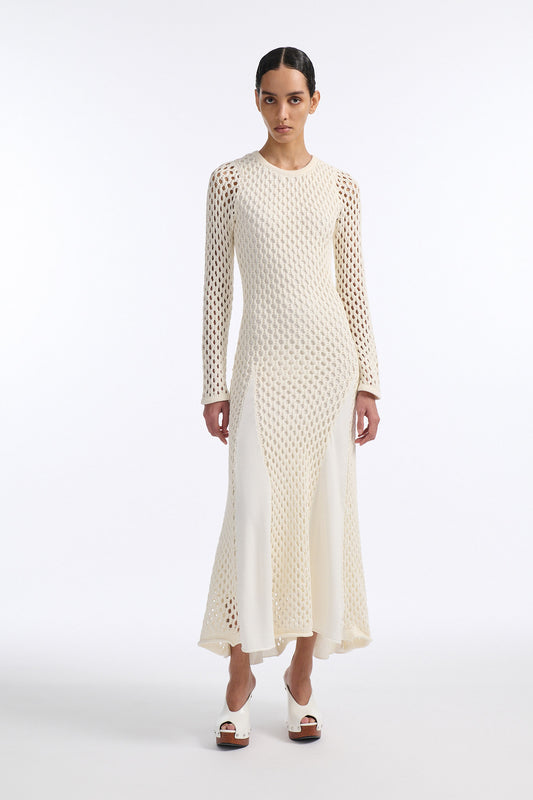 Female model with slicked back black hair in a bun wears white chunky mesh long dress. Dress has long sleeves that expose skin and a lining on the main body.