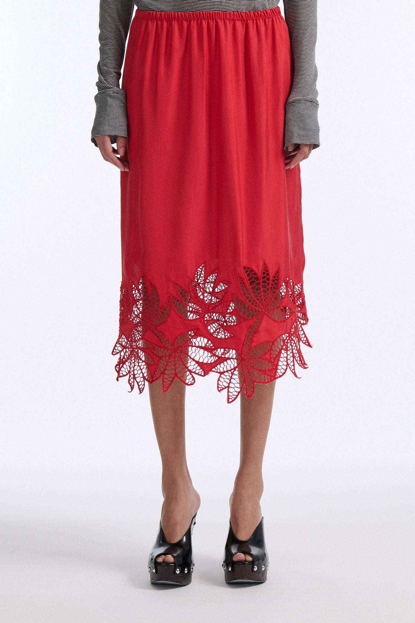 Female model with slicked back black hair in a bun wears black and grey striped fine-gauge cotton jersey long sleeve top with black mockneck crochet collar. Model also wears red silk shift skirt with palm leaf cutouts at hem. Skirt has elastic waist and is mid-length.