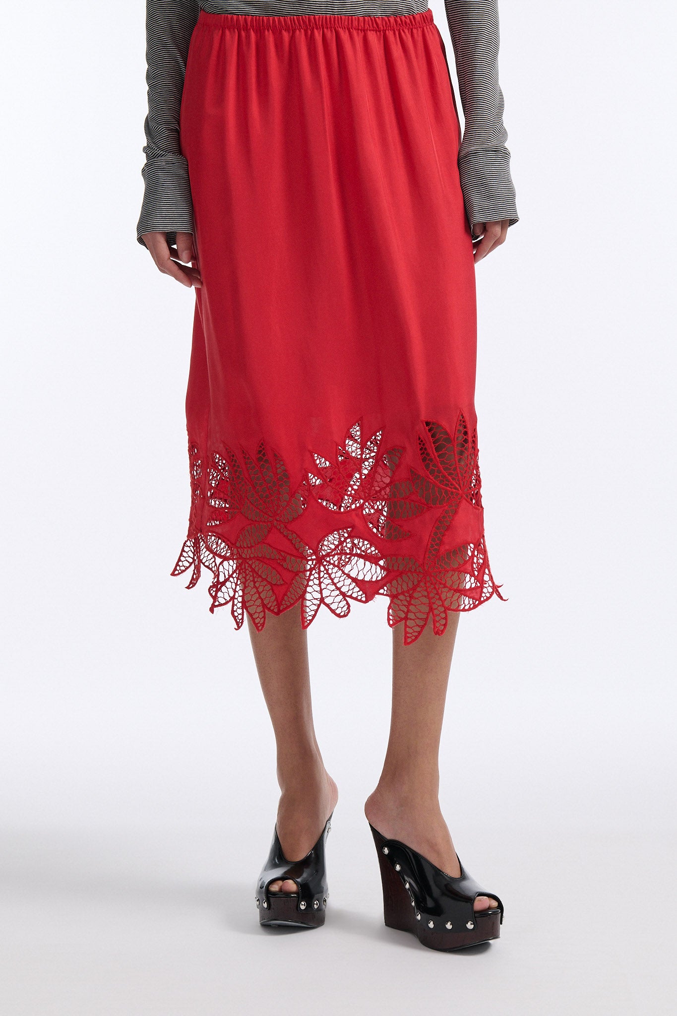 Female model with slicked back black hair in a bun wears black and grey striped fine-gauge cotton jersey long sleeve top with black mockneck crochet collar. Model also wears red silk shift skirt with palm leaf cutouts at hem. Skirt has elastic waist and is mid-length.