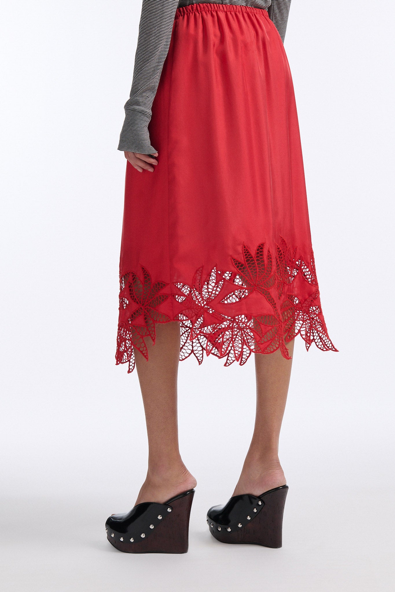 Female model with slicked back black hair in a bun wears black and grey striped fine-gauge cotton jersey long sleeve top with black mockneck crochet collar. Model also wears red silk shift skirt with palm leaf cutouts at hem. Skirt has elastic waist and is mid-length.