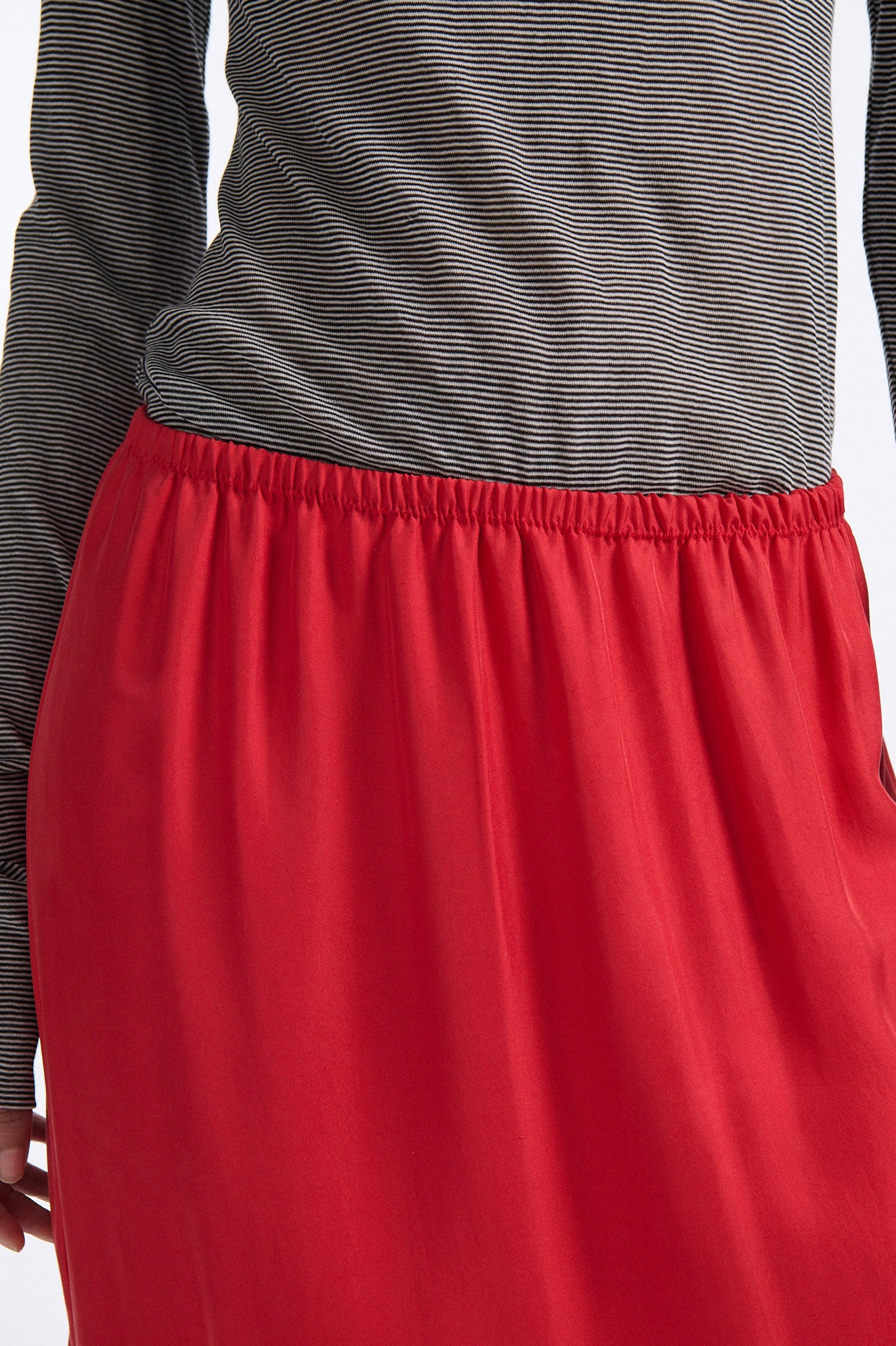 Female model with slicked back black hair in a bun wears black and grey striped fine-gauge cotton jersey long sleeve top with black mockneck crochet collar. Model also wears red silk shift skirt with palm leaf cutouts at hem. Skirt has elastic waist and is mid-length.