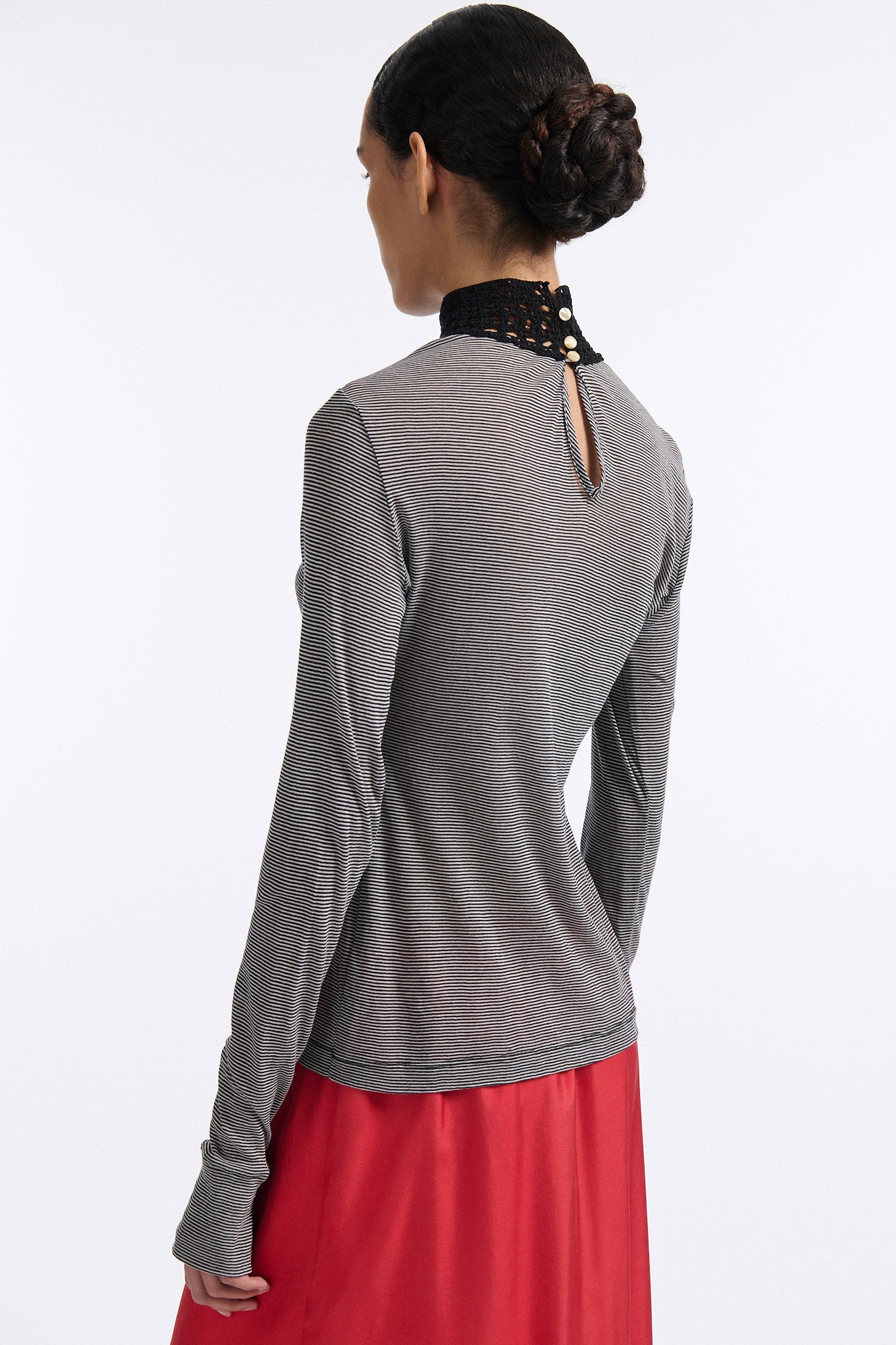 Female model with slicked back black hair in a bun wears black and grey striped fine-gauge cotton jersey long sleeve top with black mockneck crochet collar. Model also wears red silk shift skirt with palm leaf cutouts at hem and elastic waist.