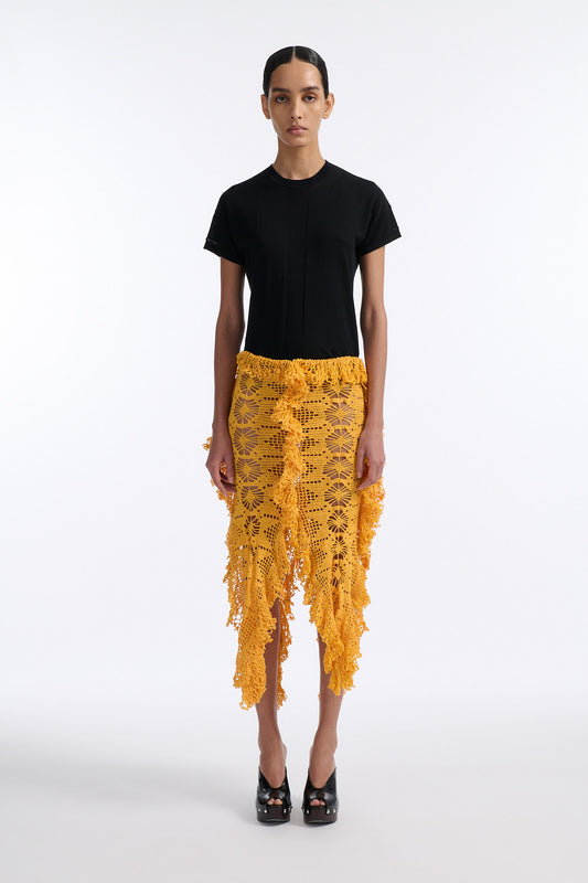 Female model with slicked back black hair in a bun wears black fine gauge cotton shirt with golden-yellow 4 panel crochet shirt. Skirt has elastic waist and crochet fringe finishing at all hems.