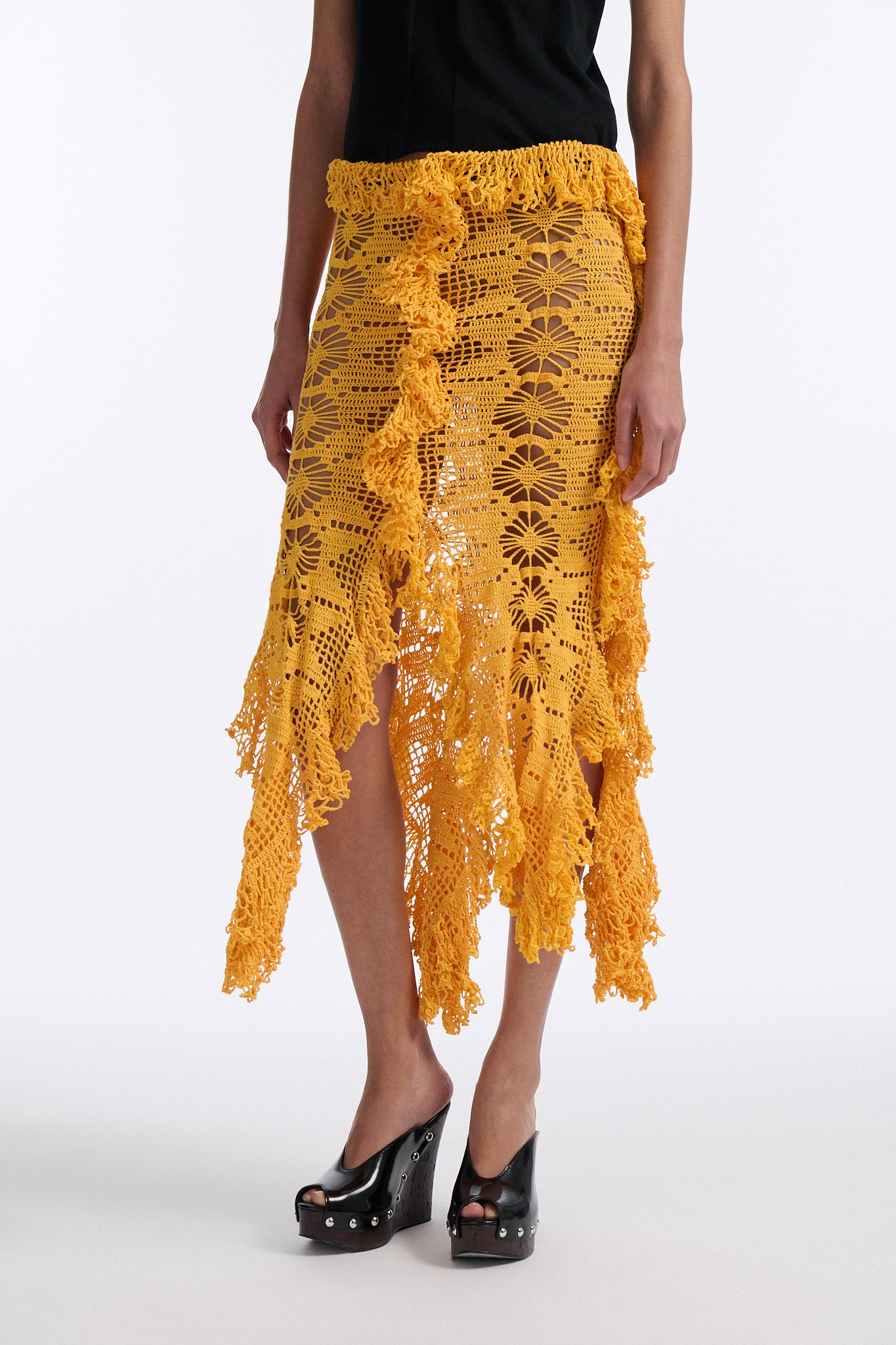 Female model with slicked back black hair in a bun wears black fine gauge cotton shirt with golden-yellow 4 panel crochet shirt. Skirt has elastic waist and crochet fringe finishing at all hems.