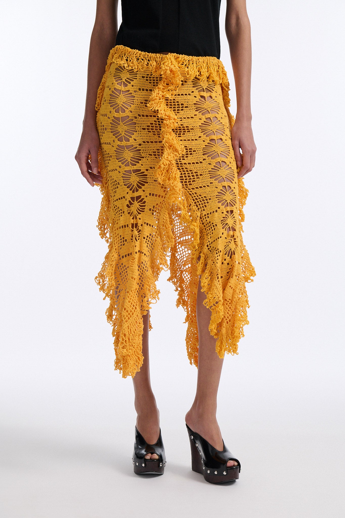 Female model with slicked back black hair in a bun wears black fine gauge cotton shirt with golden-yellow 4 panel crochet shirt. Skirt has elastic waist and crochet fringe finishing at all hems.