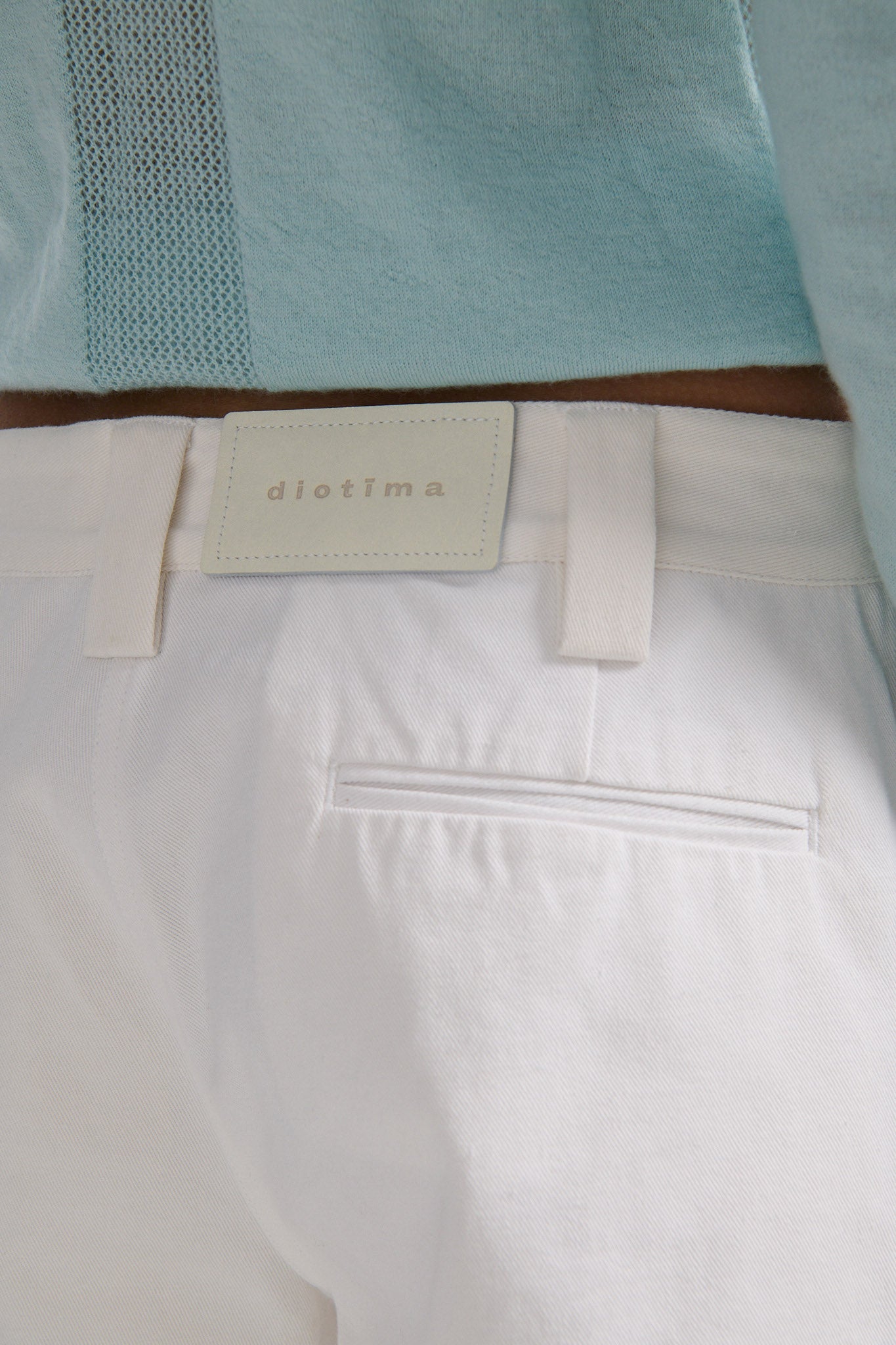 Female model with slicked back black hair in a bun wears blue fine gauge long sleeve button down cardigan and white short shorts with palm leaf cutouts at front and back.