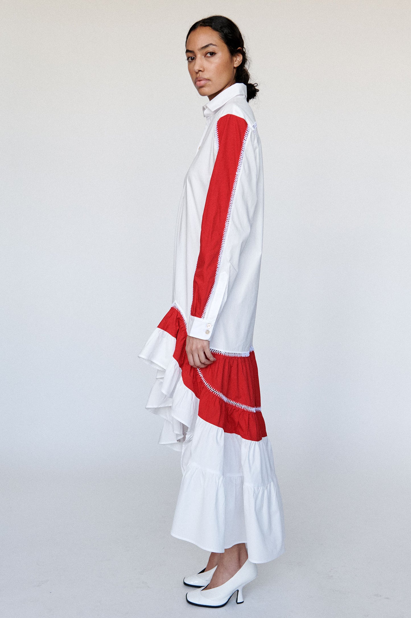 Model wears white skirt dress with hand stitched red accent panelling and gathered ruffle hem with white pump.