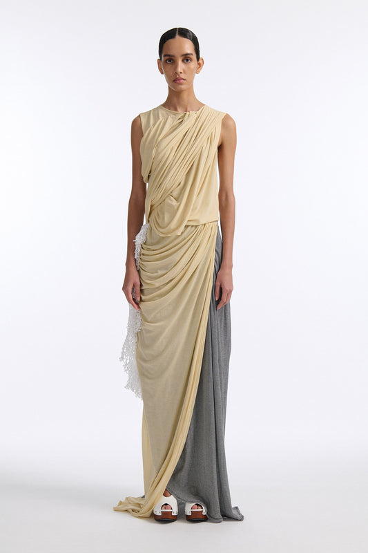 Female model with slicked back black hair in a bun wears fine gauge cotton jersey draped sleeveless gown. Draping goes diagonally across chest and gathers at waist. More diagonal draping on the lower half connects to white crochet at the hip. The front of the dress is beige and the back is horizontal black and white fine stripes.
