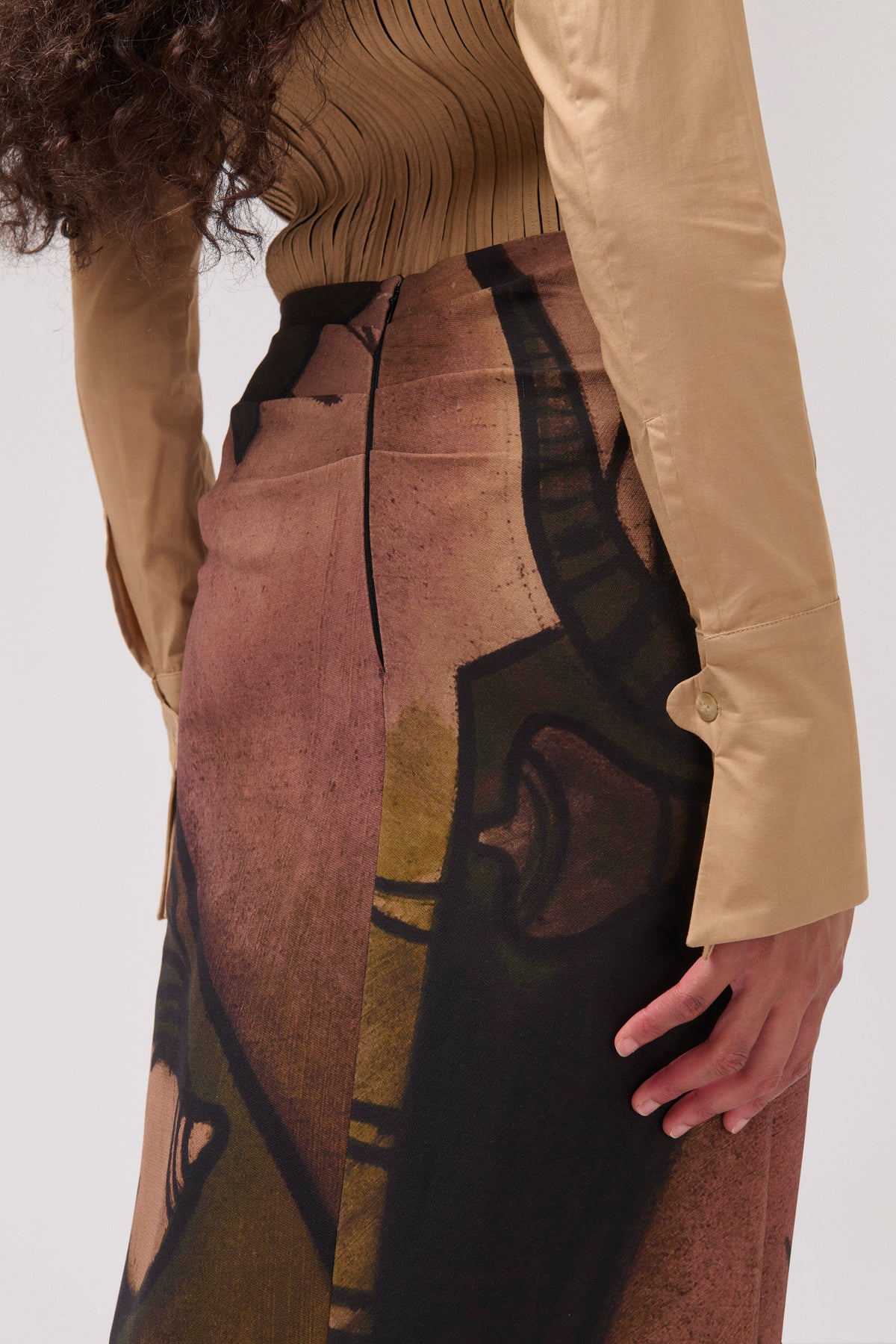 A close-up of a model wearing a high-waisted midi skirt with an abstract art print in brown, beige, and black, paired with a beige long-sleeve top.