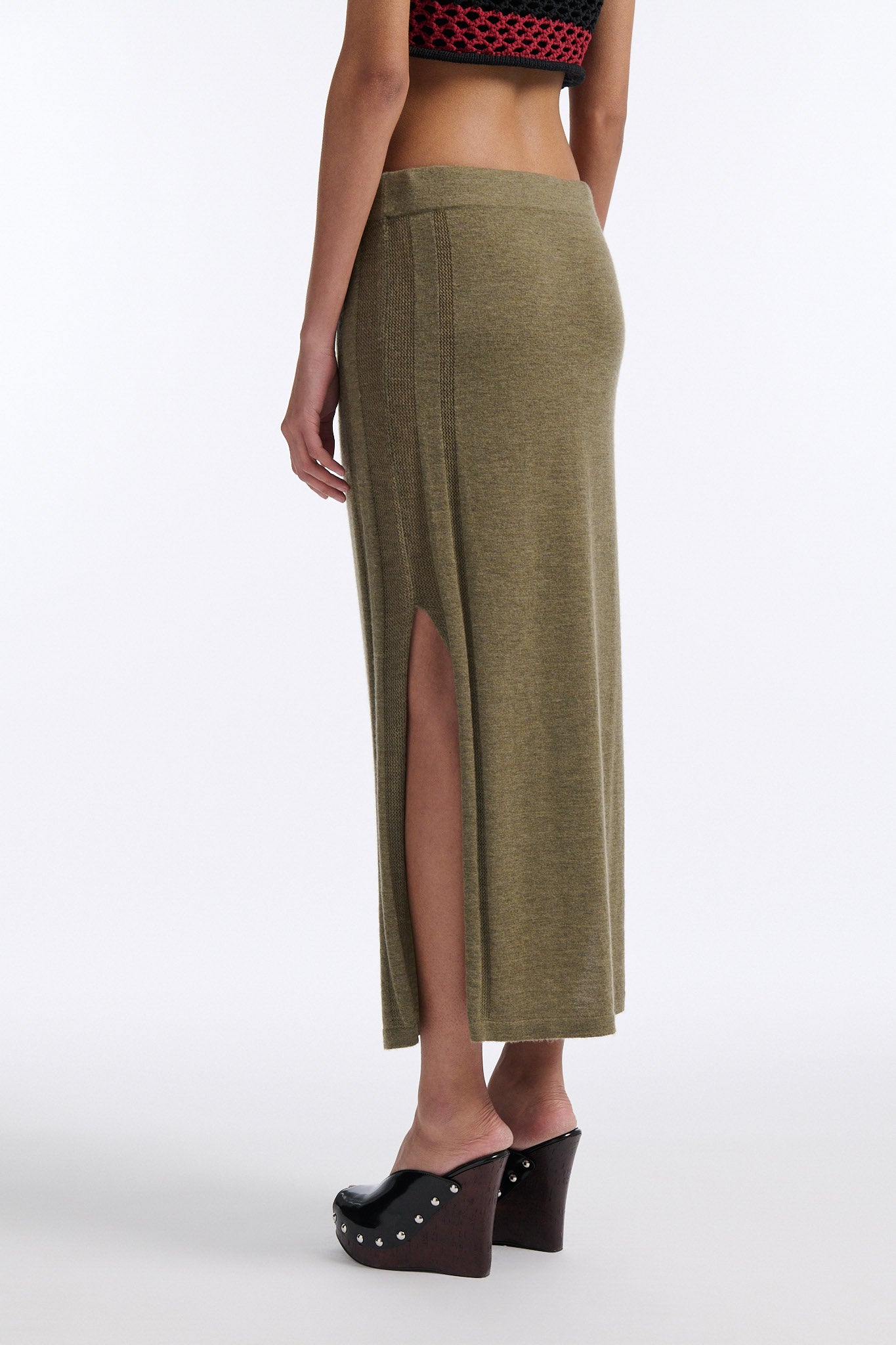 Female model with slicked back black hair in a bun wears chunky mesh horizontal striped cropped tee in red and black. The model also wears a fine gauge drawstring cashmere skirt with pointelle stitching on either side and a long slit on either side.