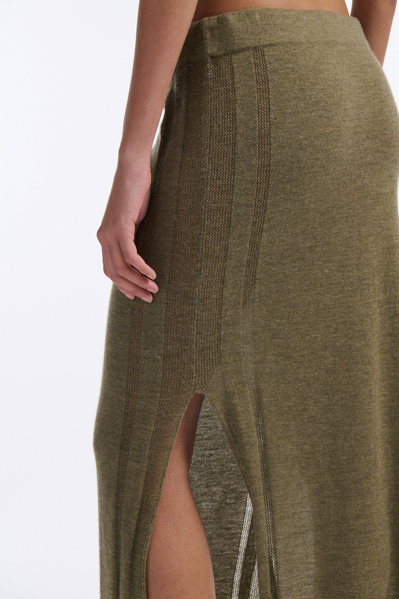 Female model with slicked back black hair in a bun wears chunky mesh horizontal striped cropped tee in red and black. The model also wears a fine gauge drawstring cashmere skirt with pointelle stitching on either side and a long slit on either side.