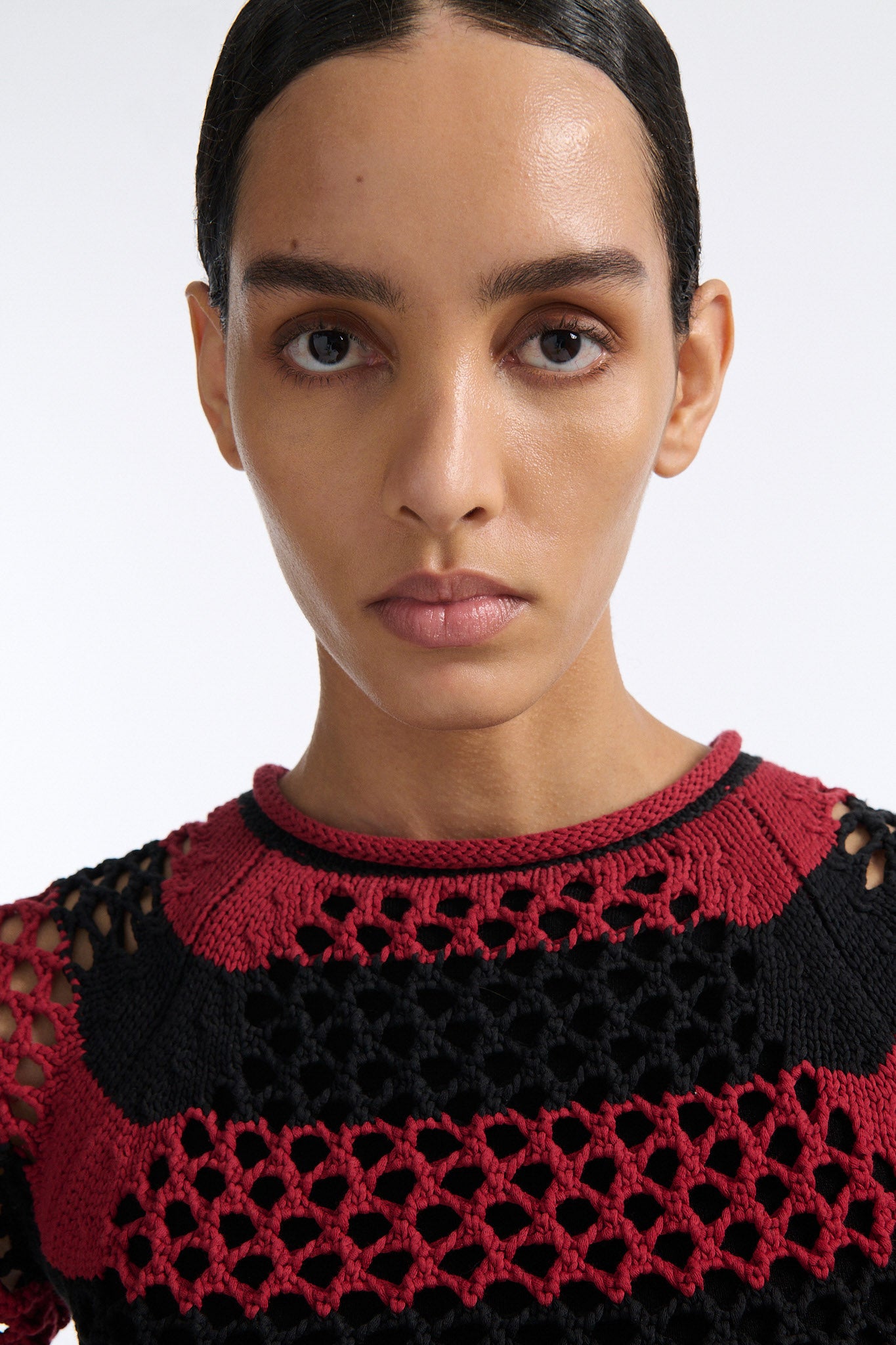 Female model with slicked back black hair in a bun wears red and black bold striped mesh tee, cropped above the belly button, and mid-waist long adjustable skirt in soft green cashmere with black platform wedges.