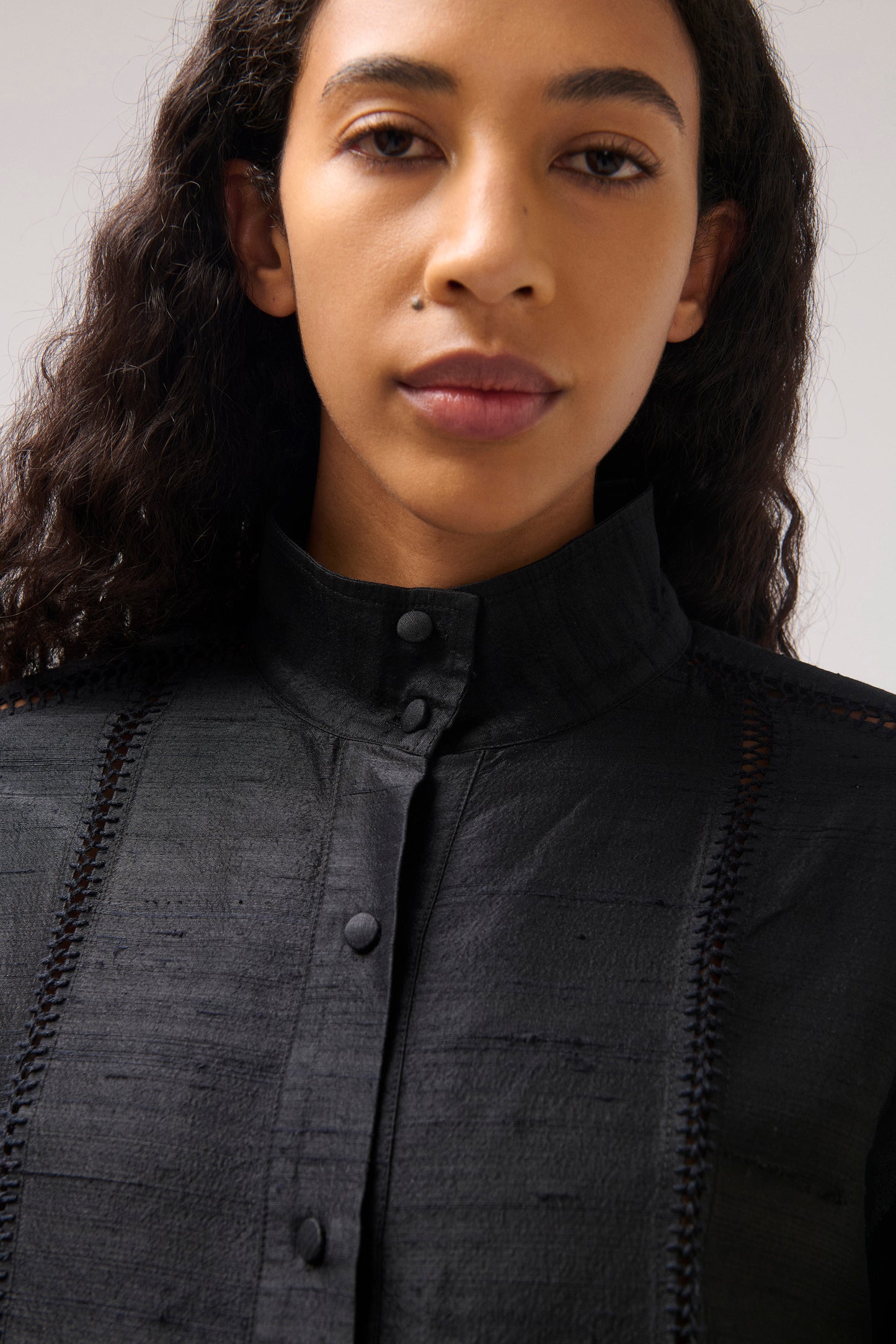 Close-up of a model wearing a black textured high-neck button-up shirt with decorative vertical stitching details.