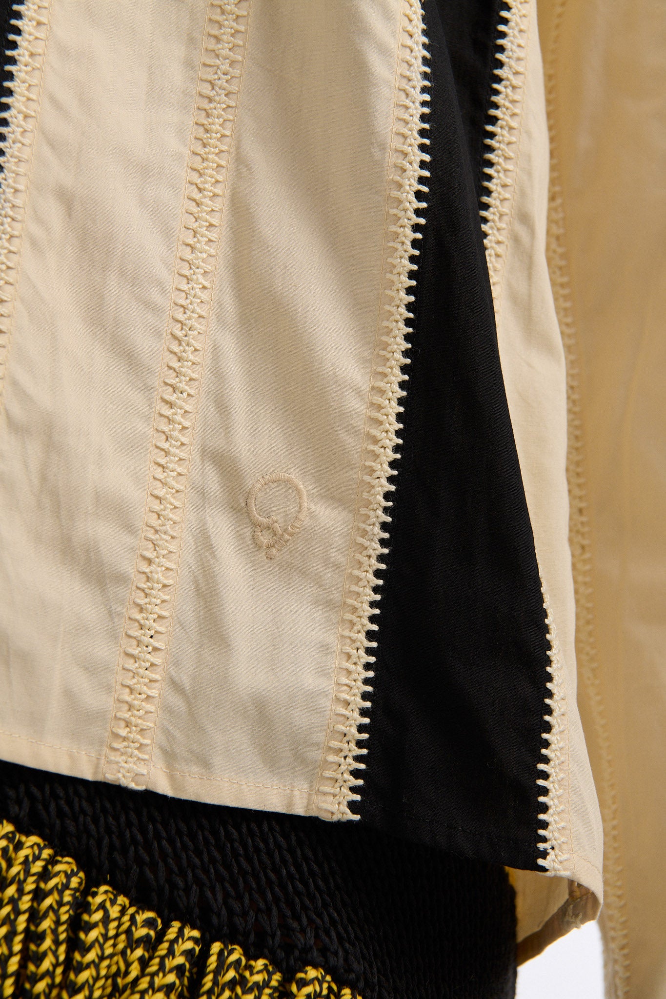 Female model with slicked back black hair in a bun wears ivory and black wide vertical stripe collared shirt. Shirt is wide cut with slight crop. Model also wears mixed stitch mesh skirt made in a yellow and black yarn with long fringe hem.