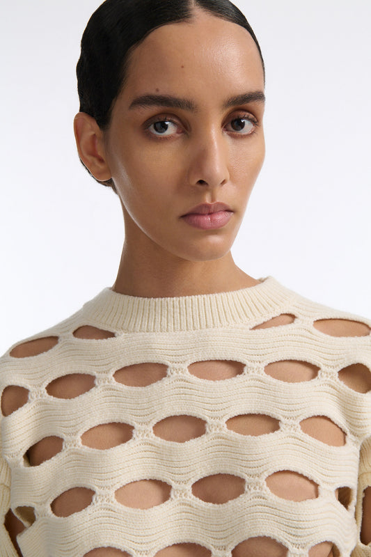 Female model with slicked back black hair in a bun wears black linen shorts with vertical shell embellishments on the front. The shorts have a 2 inch inseam and are worn with an allover cutout off-white sweater.