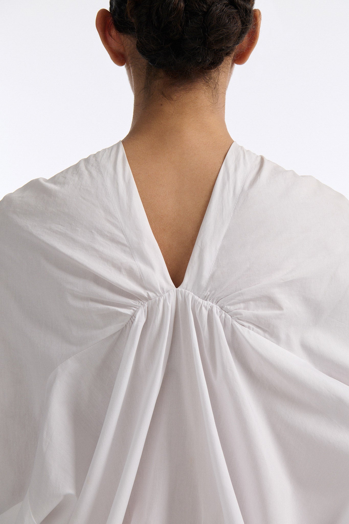 Female model with slicked back black hair in a bun wears white gathered V-neck blouse with puff sleeves and drawstring at waist. Model also wears bright orange chunky mesh skirt with clear crystal hand-sewn embellishments.