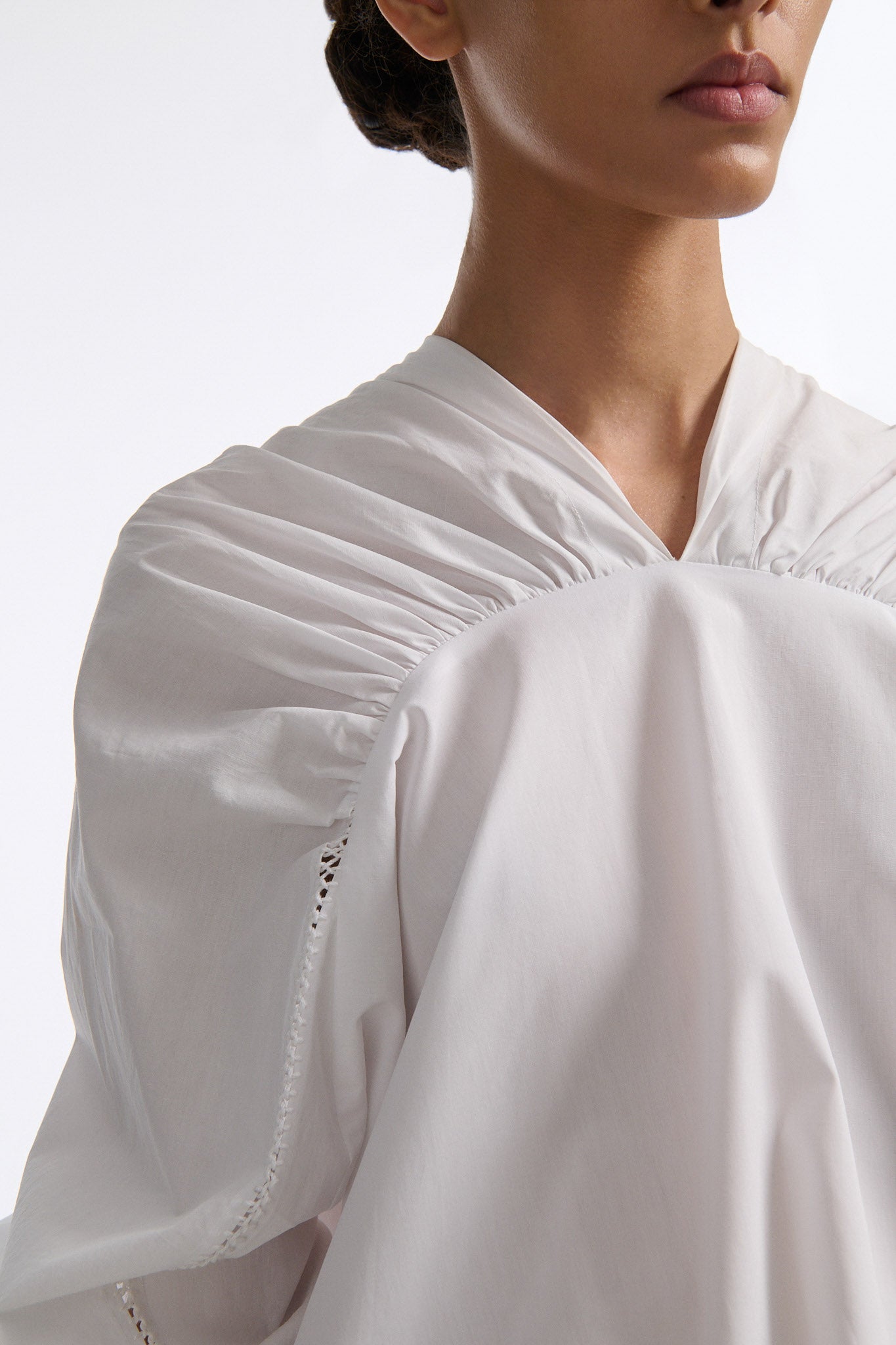 Female model with slicked back black hair in a bun wears white gathered V-neck blouse with puff sleeves and drawstring at waist. Model also wears bright orange chunky mesh skirt with clear crystal hand-sewn embellishments.