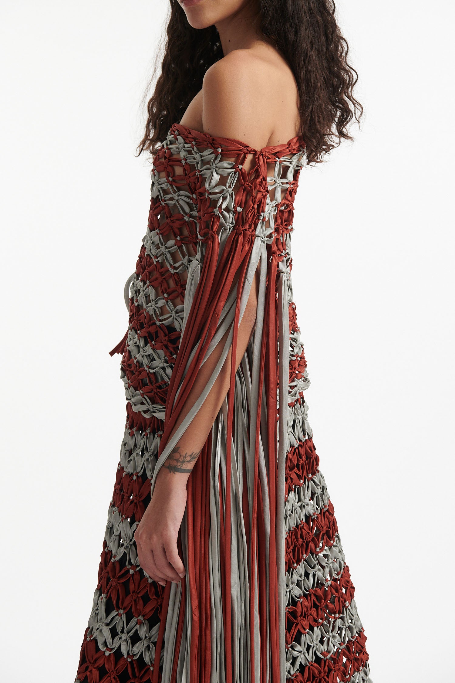 Female model wears knotted macrame set in burnt orange and sky grey. Both the top and skirt have asymmetric fringe hanging down either side. Model is on a white background.