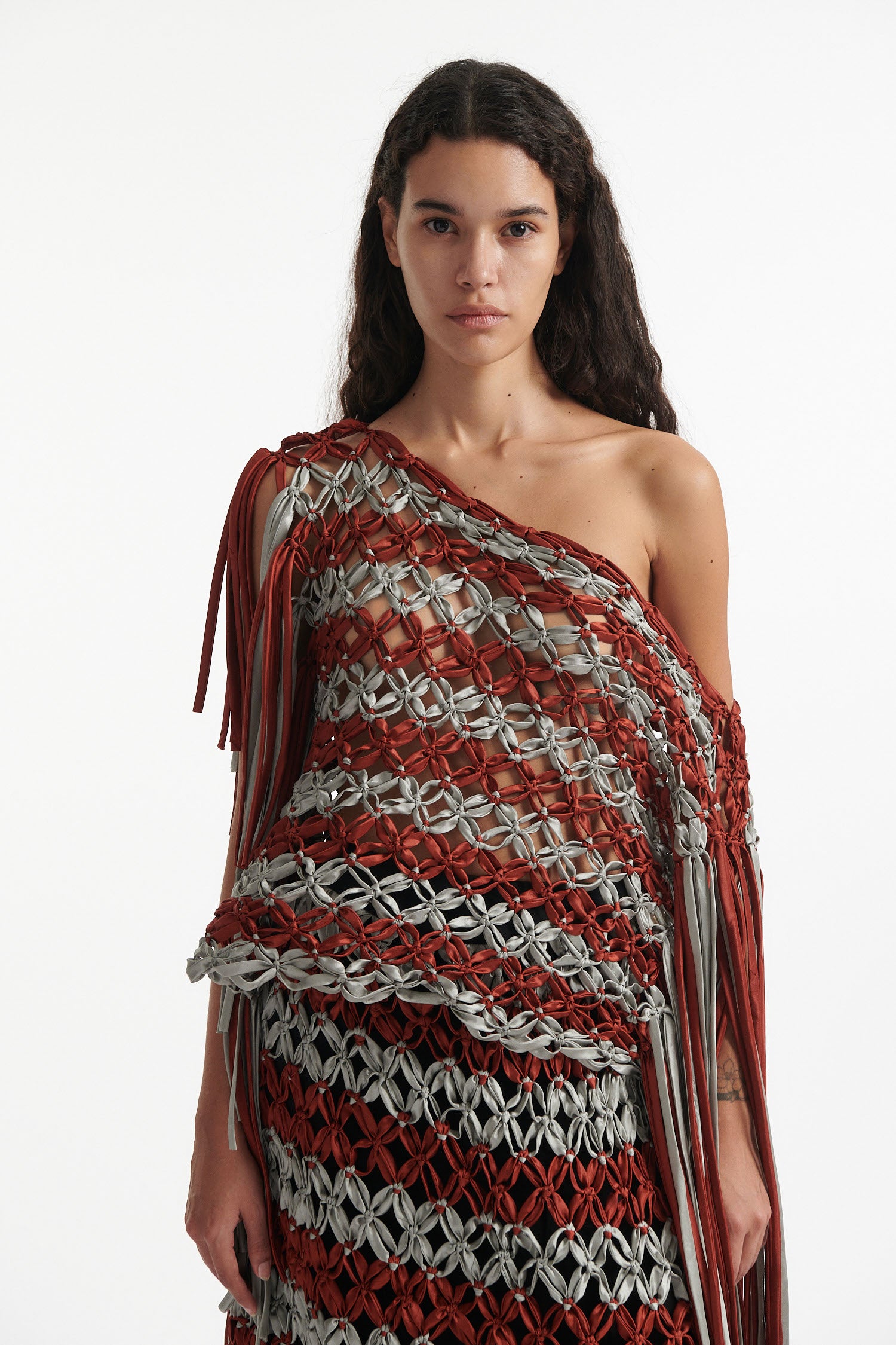 Female model wears knotted macrame set in burnt orange and sky grey. Both the top and skirt have asymmetric fringe hanging down either side. Model is on a white background.