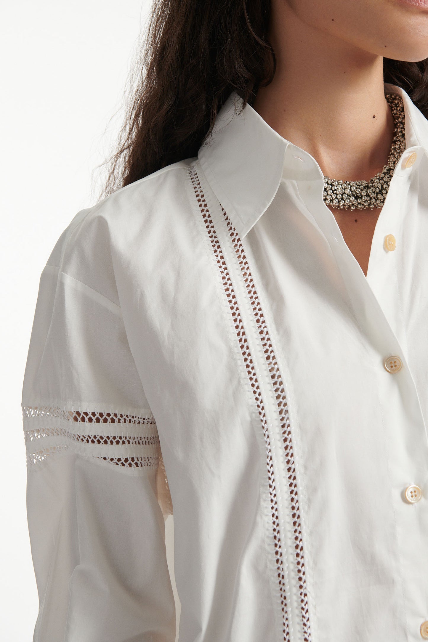 Female model wears white poplin shirt with exposed stitches and black high heel boots on white background.