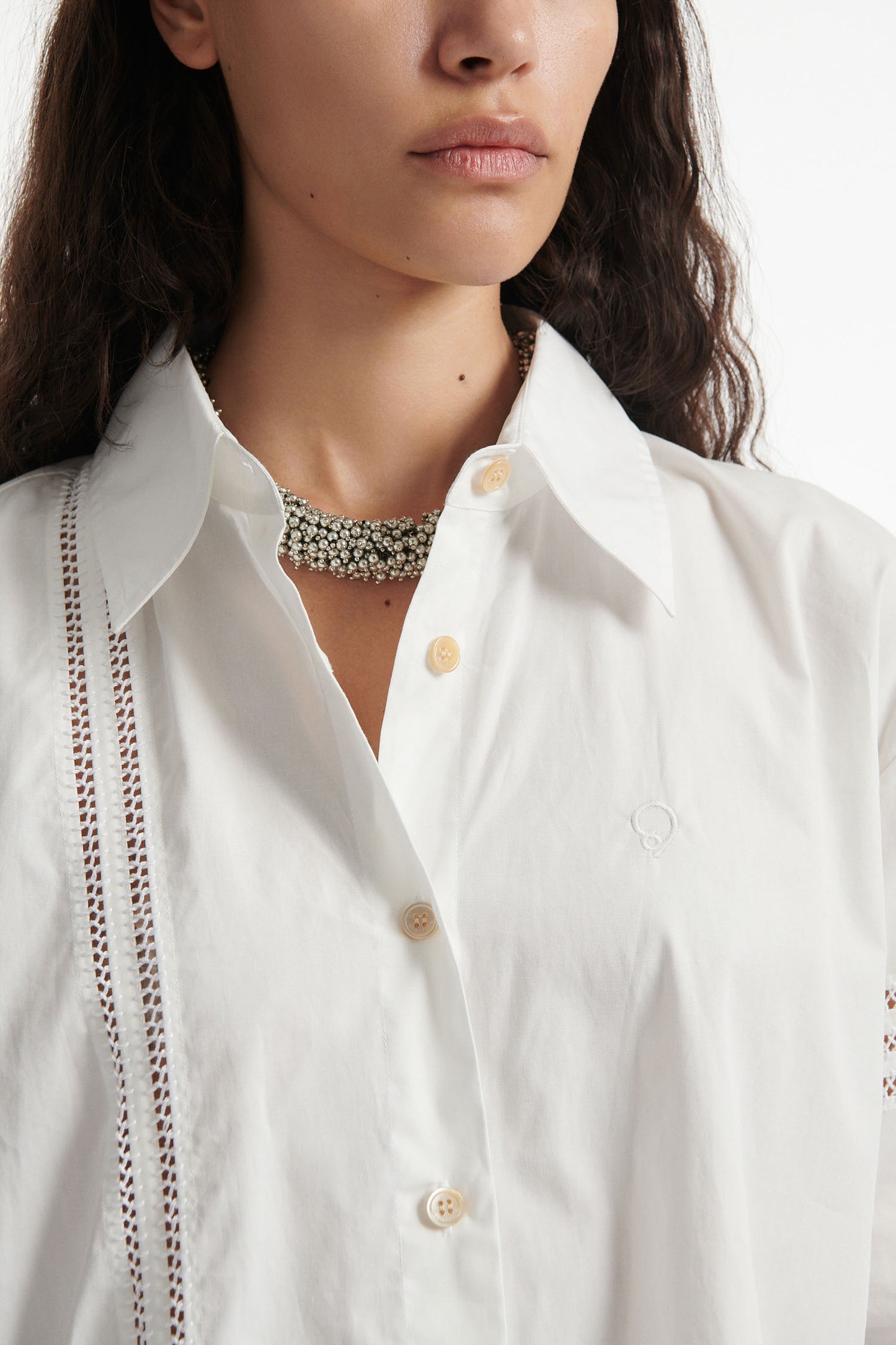 Female model wears white poplin shirt with exposed stitches and black high heel boots on white background.