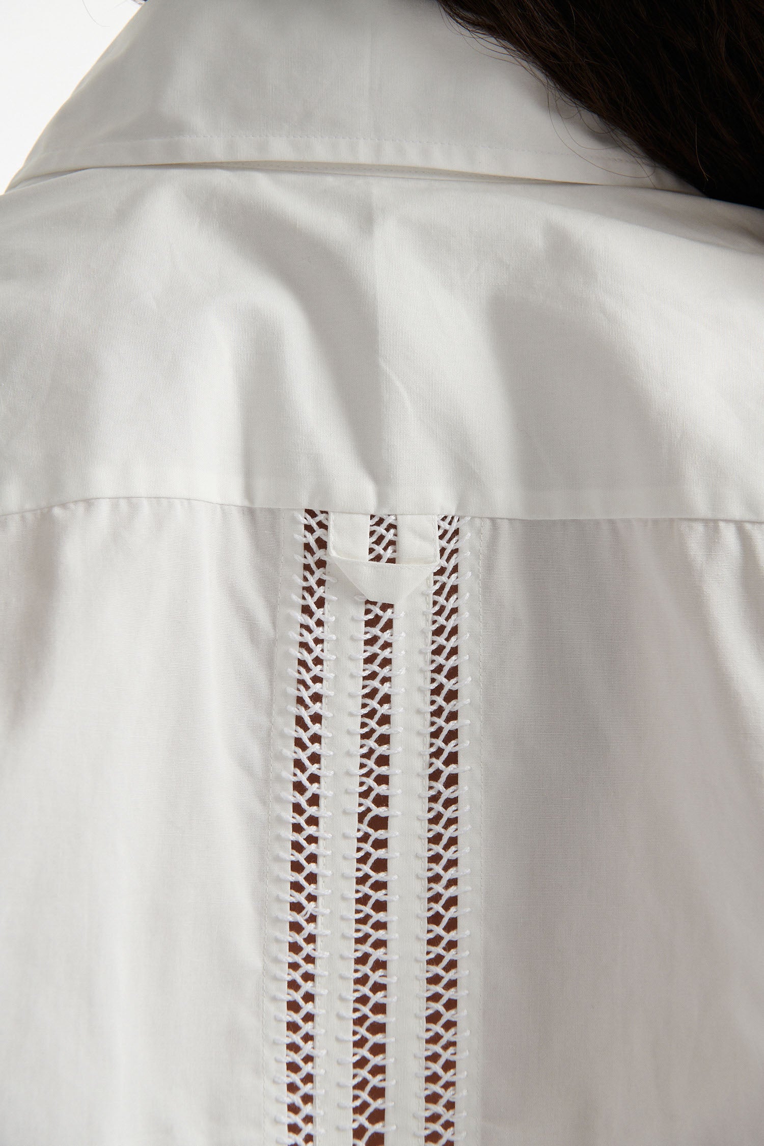 Female model wears white poplin shirt with exposed stitches and black high heel boots on white background.