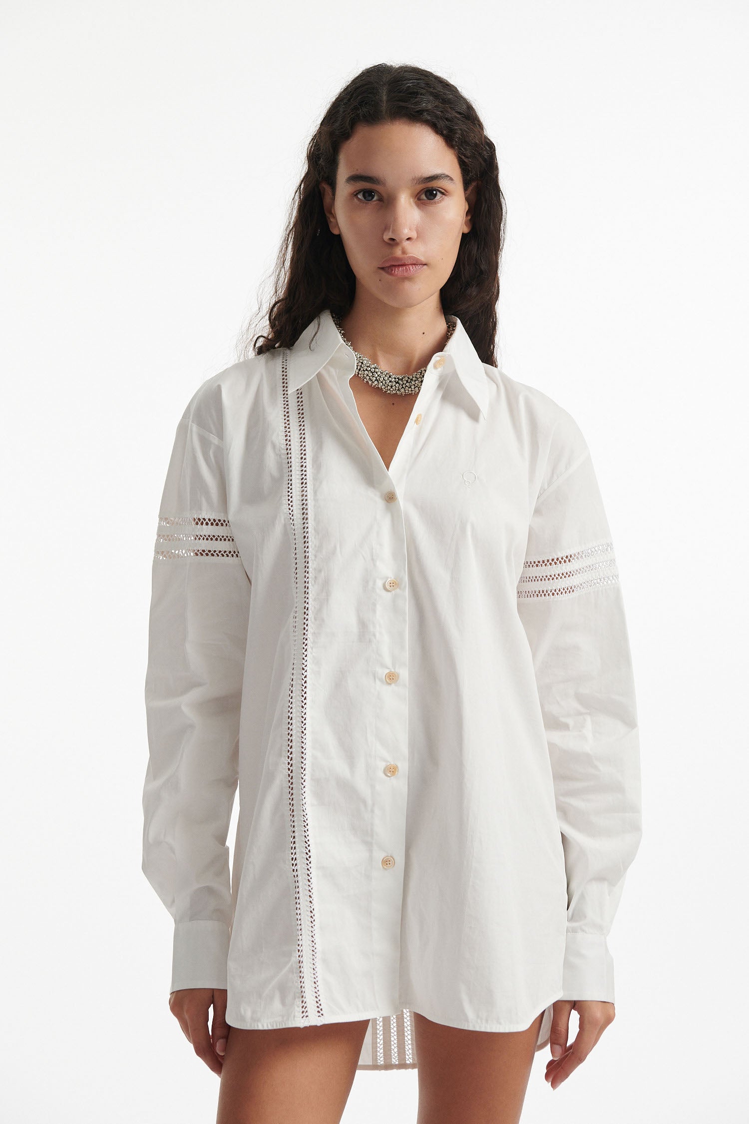 Female model wears white poplin shirt with exposed stitches and black high heel boots on white background.