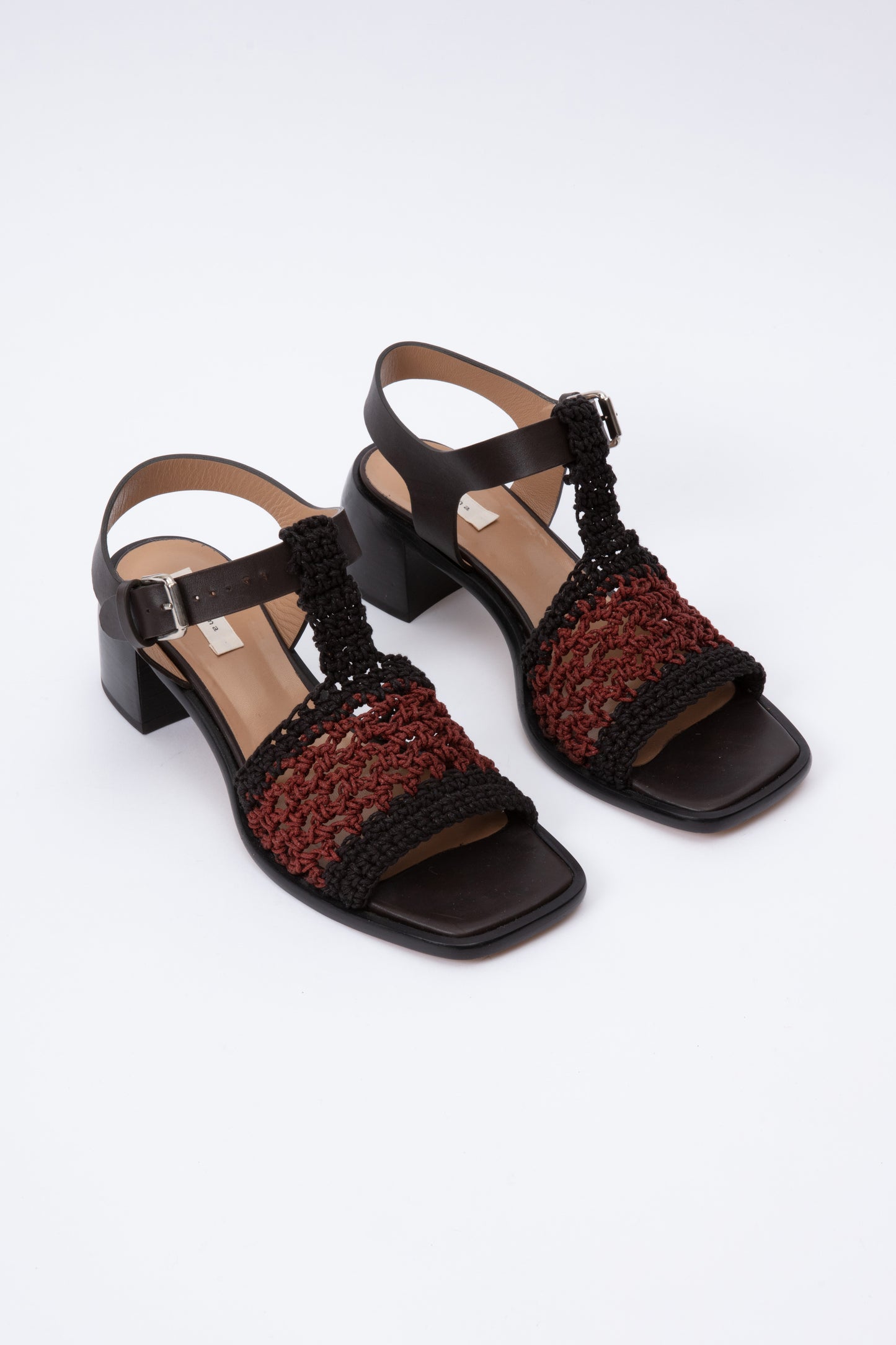 Open toe sandals with black leather base and ankle straps. The block heel is slightly rounded and thick. Connected to the ankle strap is a toe strap made from hand-knit crochet in black and maroon.