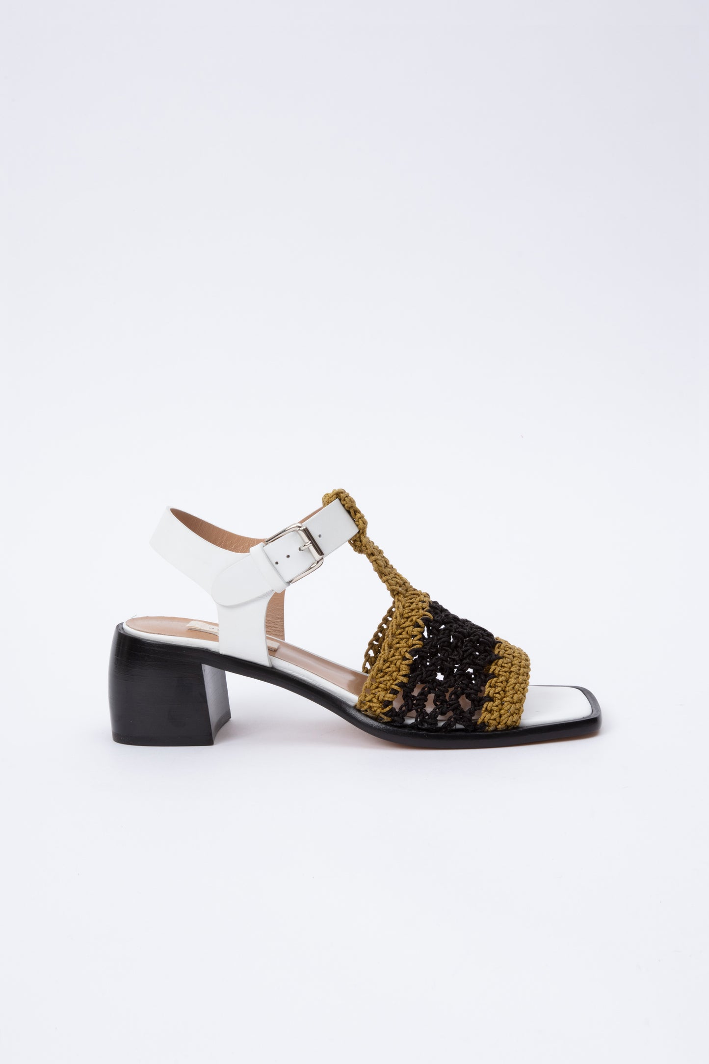 Open toe sandals with black leather base and white leather ankle straps. The block heel is slightly rounded and thick. Connected to the ankle strap is a toe strap made from hand-knit crochet in a cumin yellow and black.