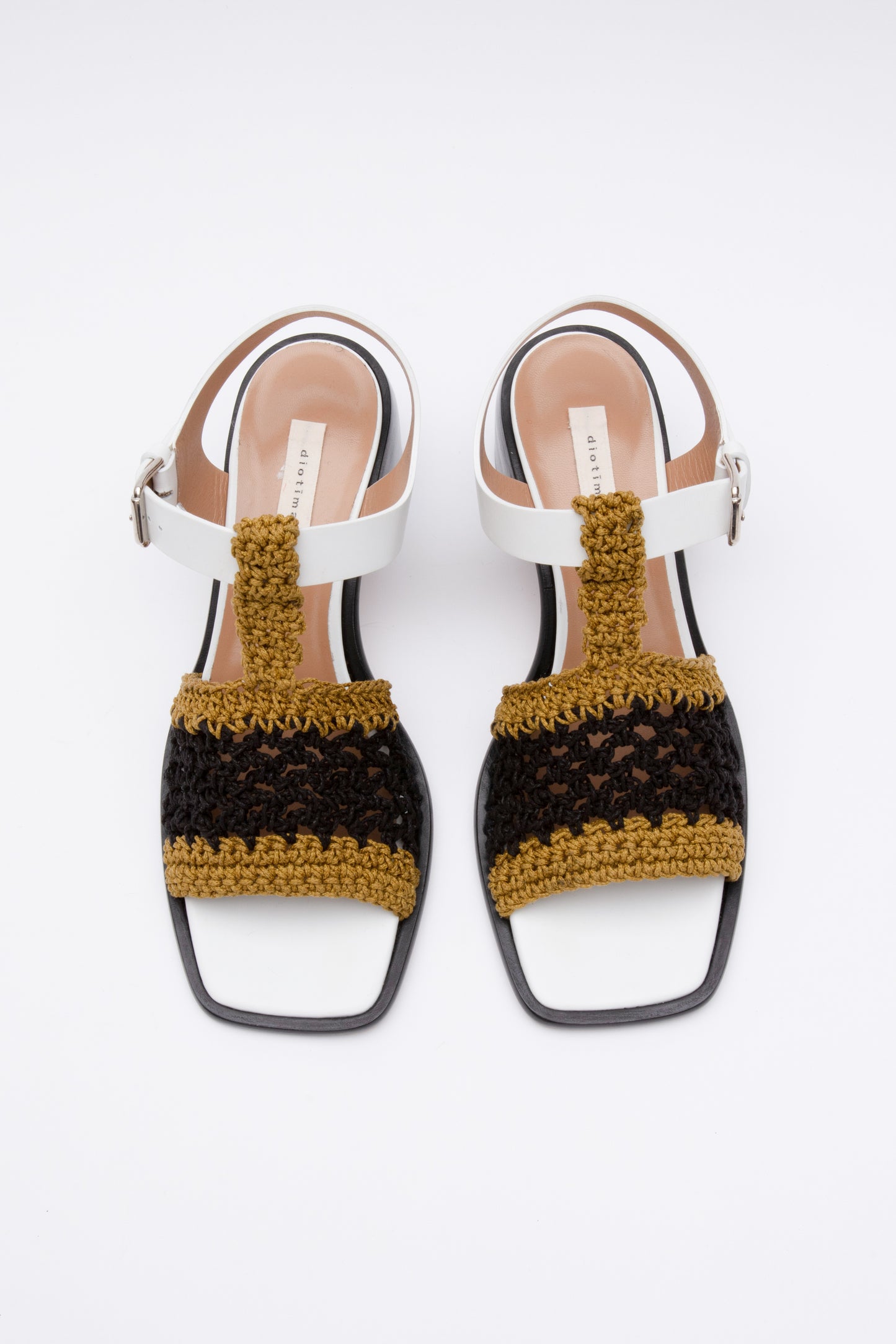 Open toe sandals with black leather base and white leather ankle straps. The block heel is slightly rounded and thick. Connected to the ankle strap is a toe strap made from hand-knit crochet in a cumin yellow and black.