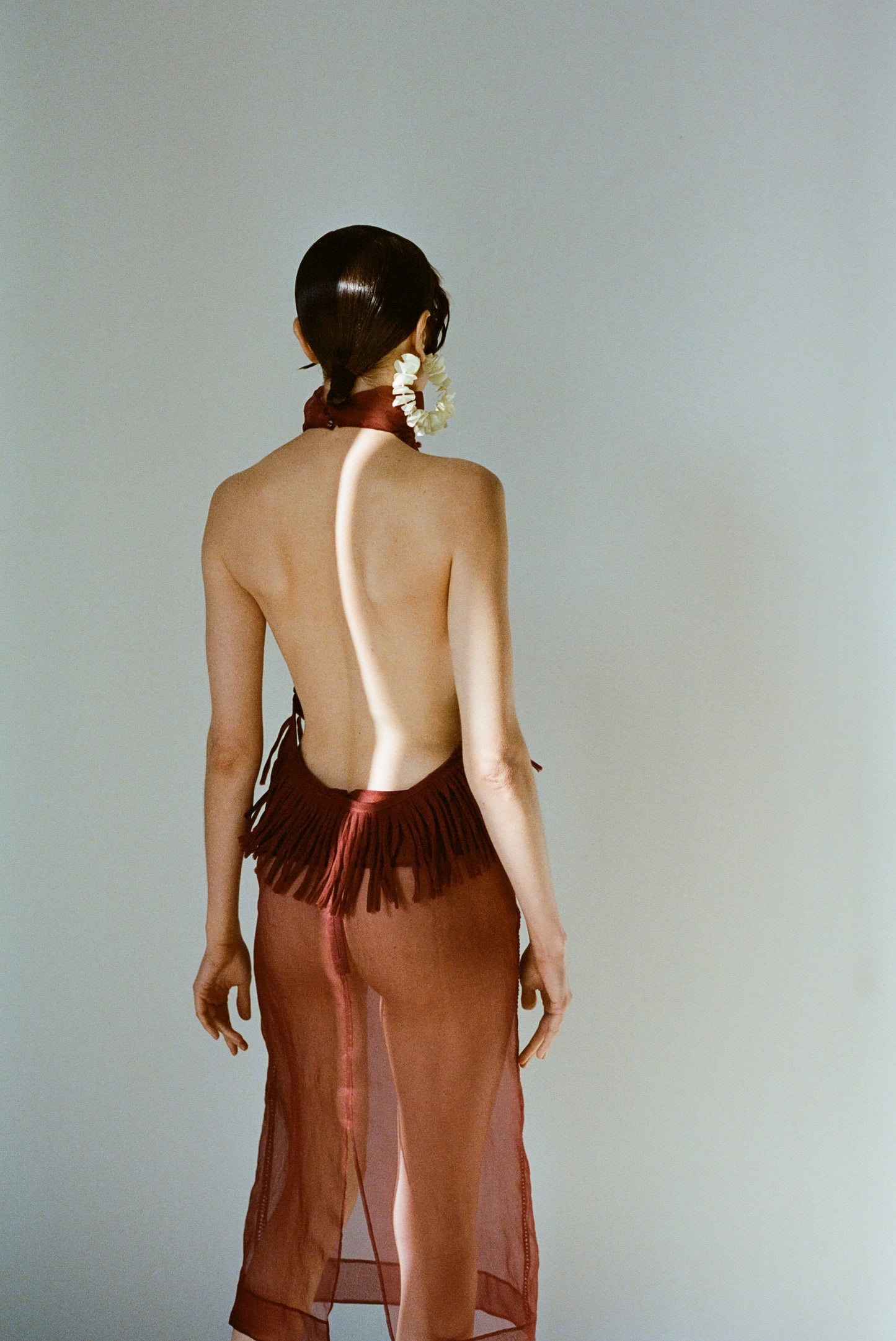 Model wearing a red sheer halter top with fringe and matching sheer midi skirt  photographed against a plain background