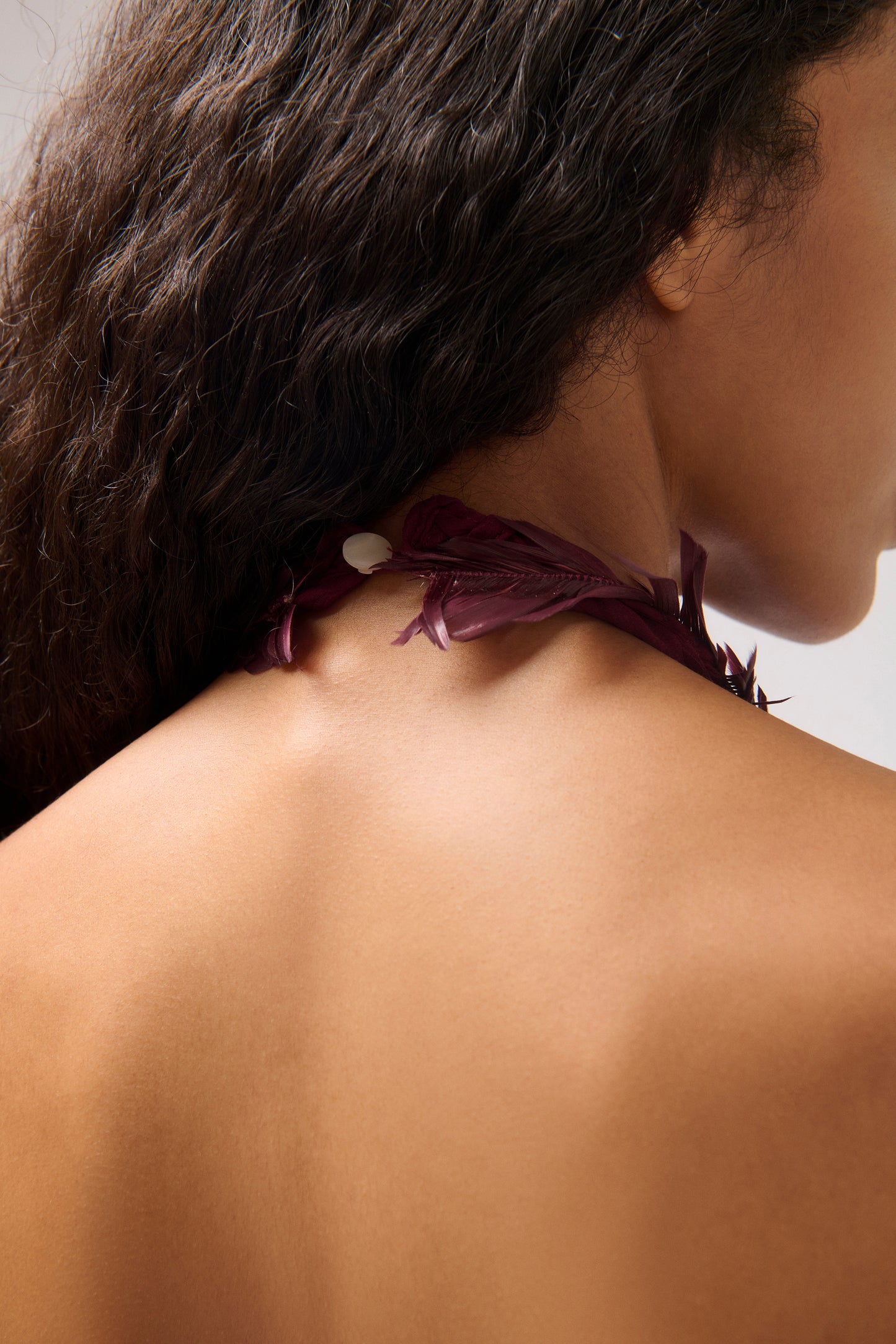 Close-up of a model's neck and upper back highlighting a dark plum feather detail.
