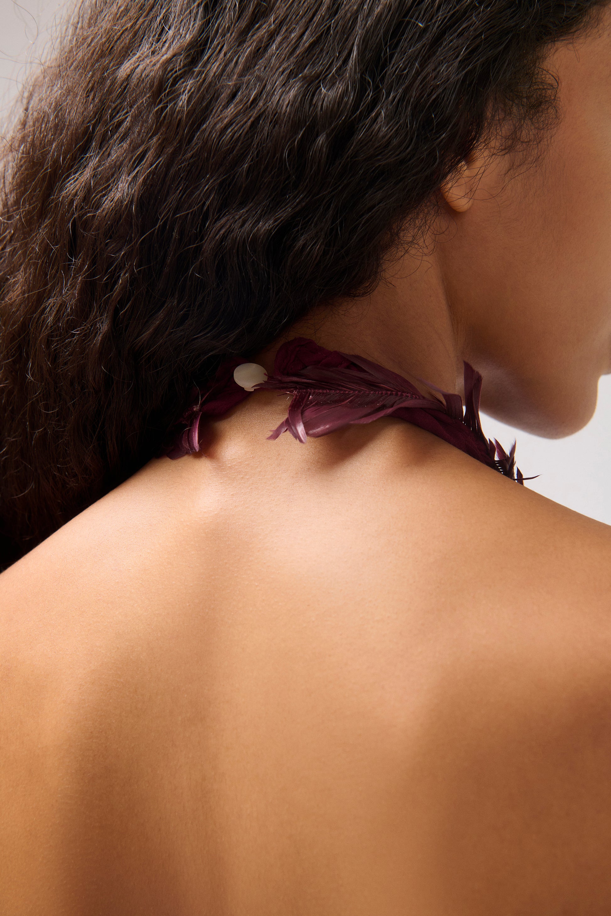 Close-up of a model's neck and upper back highlighting a dark plum feather detail.
