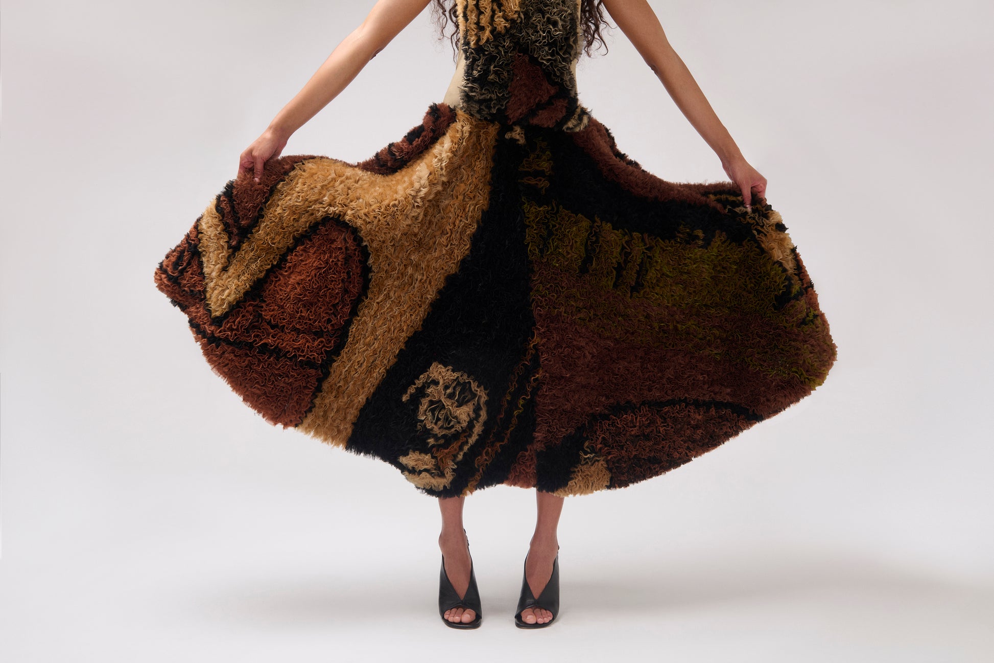 A cropped image of a model wearing a voluminous printed organza skirt. holding the skirt out against a plain light gray studio background.