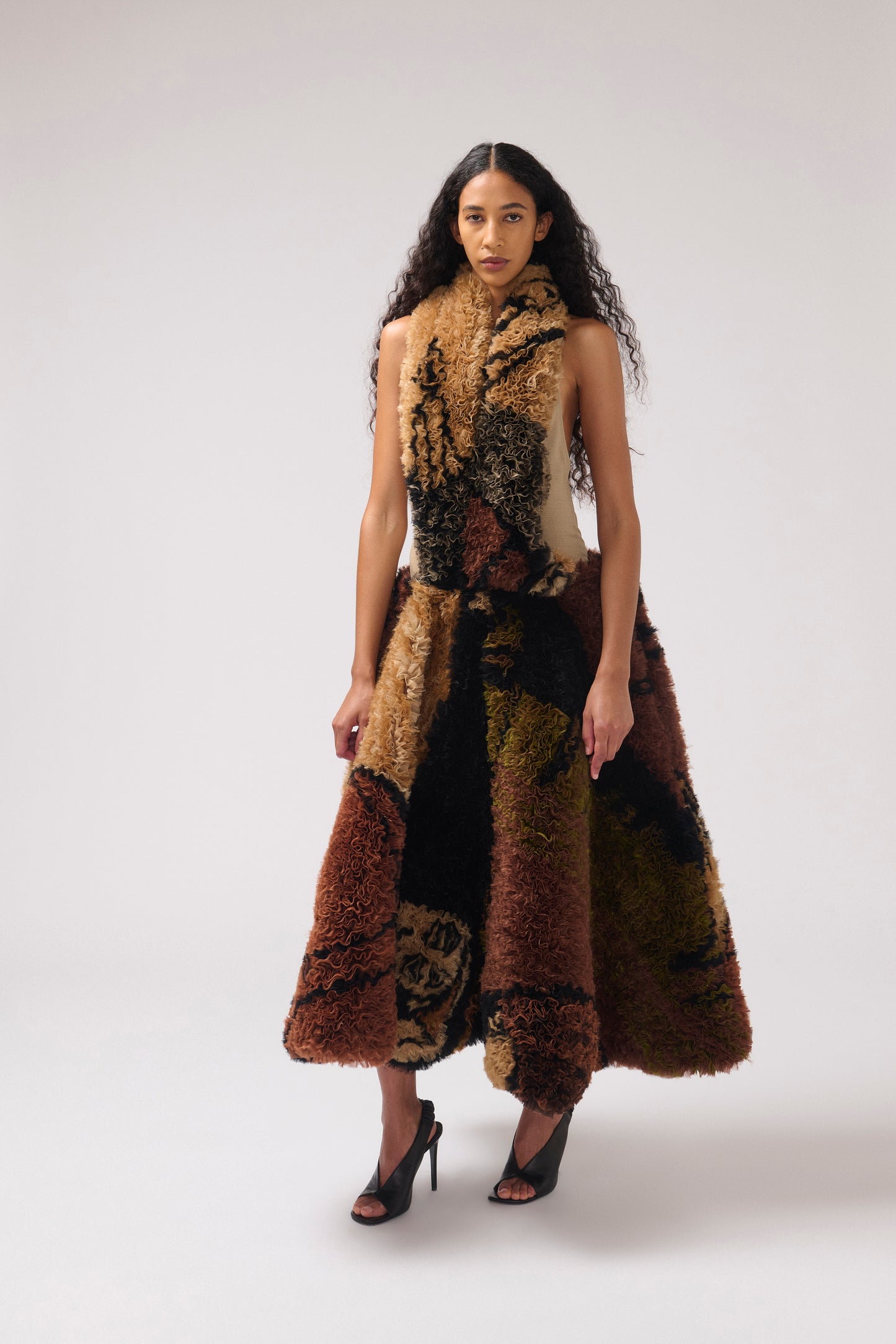 A brown and beige printed organza dress with a halter neckline, photographed worn by a model looking at the camera wearing black leather sandals.
