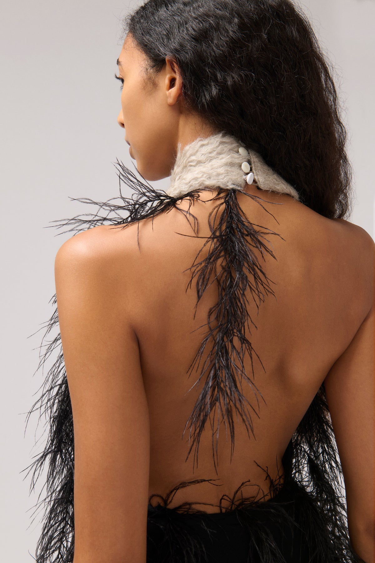 A model shown from the back wearing a beige halter dress with black feathers.