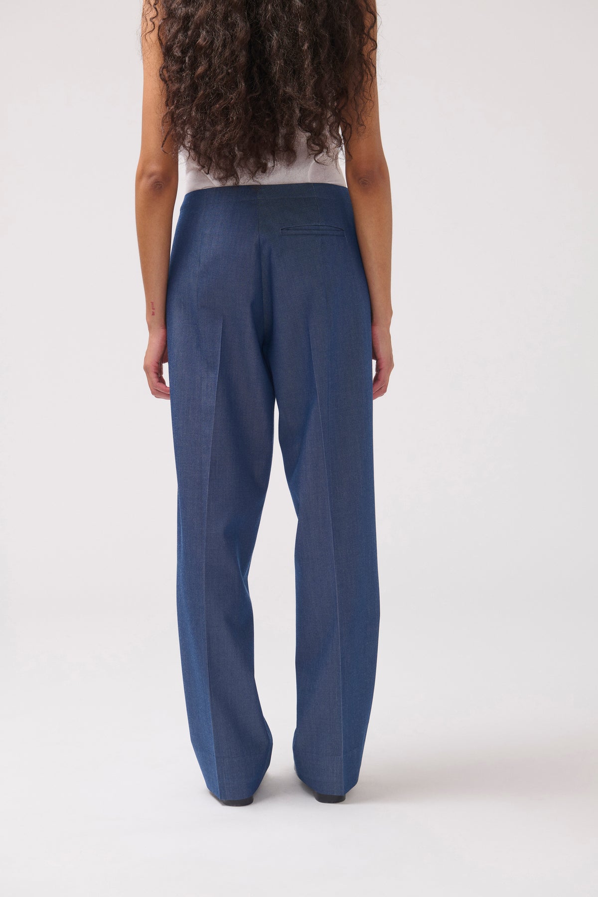 A model shown from the back wearing a pair of wide-leg blue trousers, photographed against a clean white studio background.