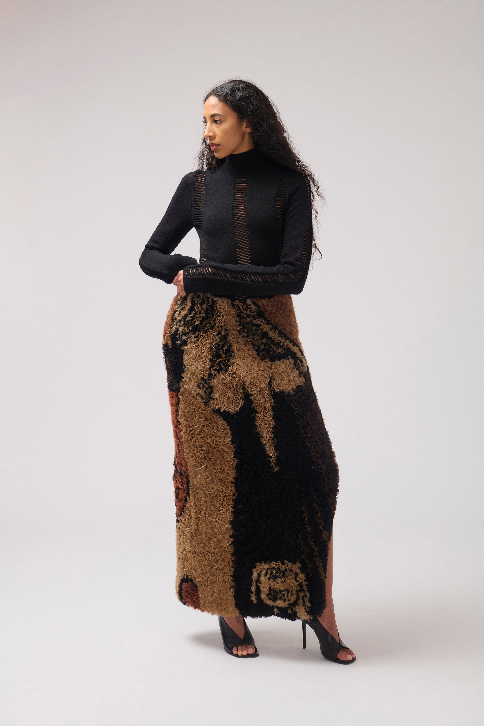 A model wearing ruffled organza striaght skirt with a dark brown and black abstract pattern, shown flat against a solid white background. Facing sideways