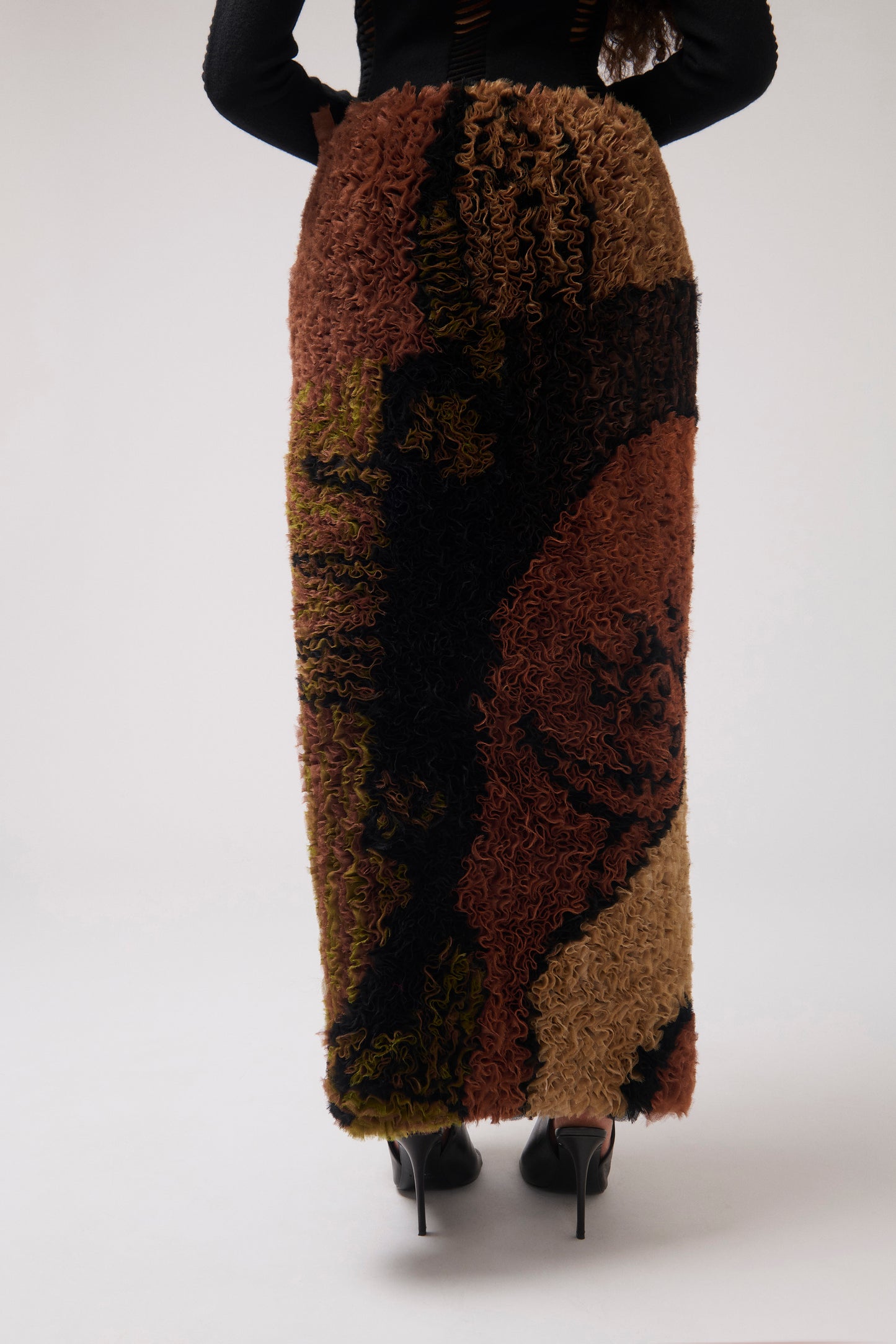A cropped image of model wearing ruffled organza striaght skirt from the back. The skirt has  a dark brown and black abstract pattern. Model shown against a solid white background.