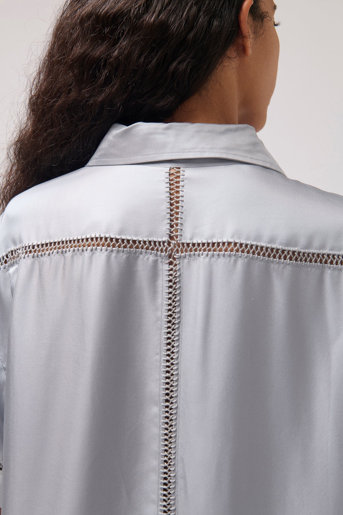 Close-up back view of a person wearing a light gray satin-like collared shirt with decorative metallic chain embroidery across the shoulders and down the center back.