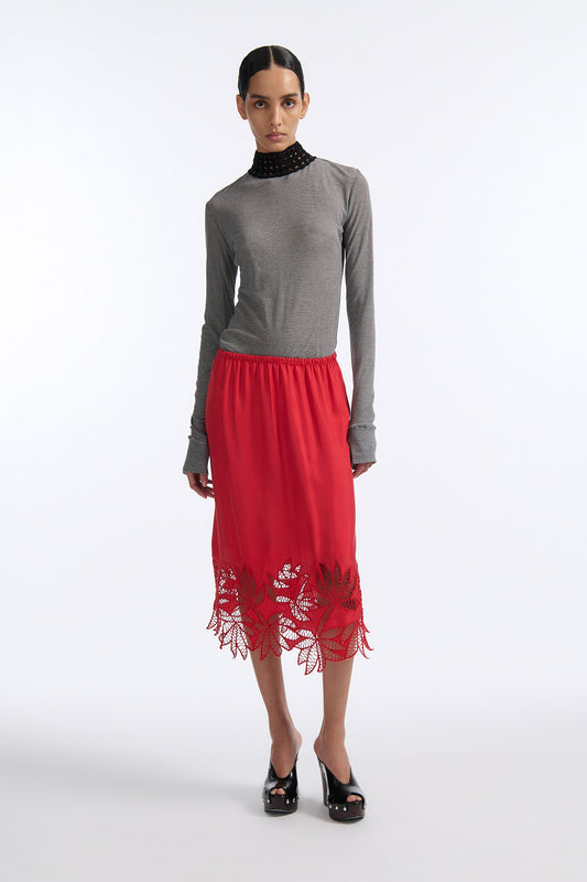 Female model with slicked back black hair in a bun wears black and grey striped fine-gauge cotton jersey long sleeve top with black mockneck crochet collar. Model also wears red silk shift skirt with palm leaf cutouts at hem. Skirt has elastic waist and is mid-length.