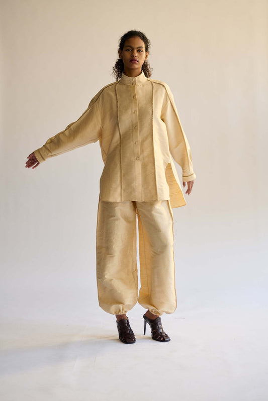 Person wearing a beige outfit with a high collar and wide-leg pants against a plain background