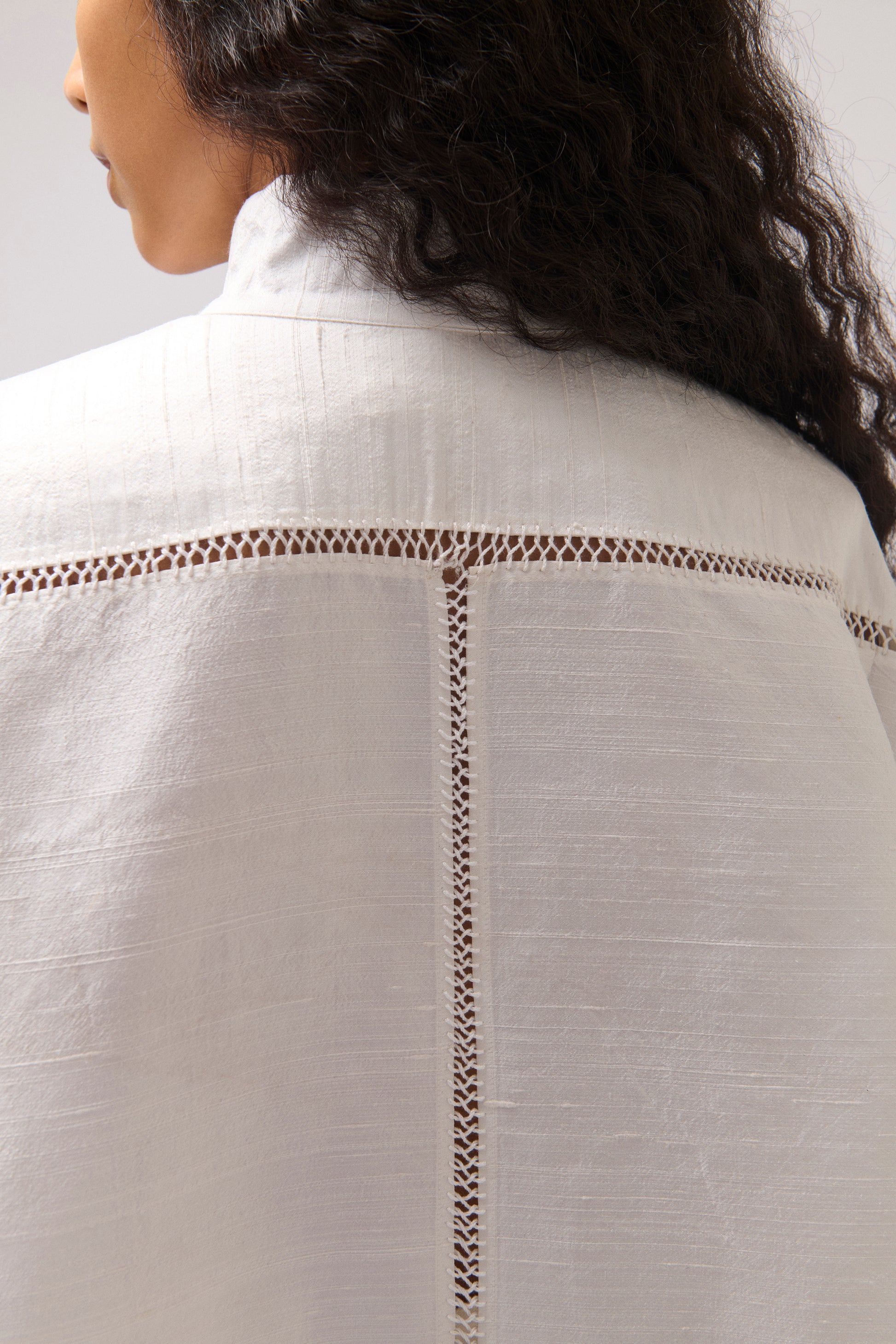 Close-up back view of a person wearing a white silk shirt with hand stitched trim across the shoulders and down the center back.