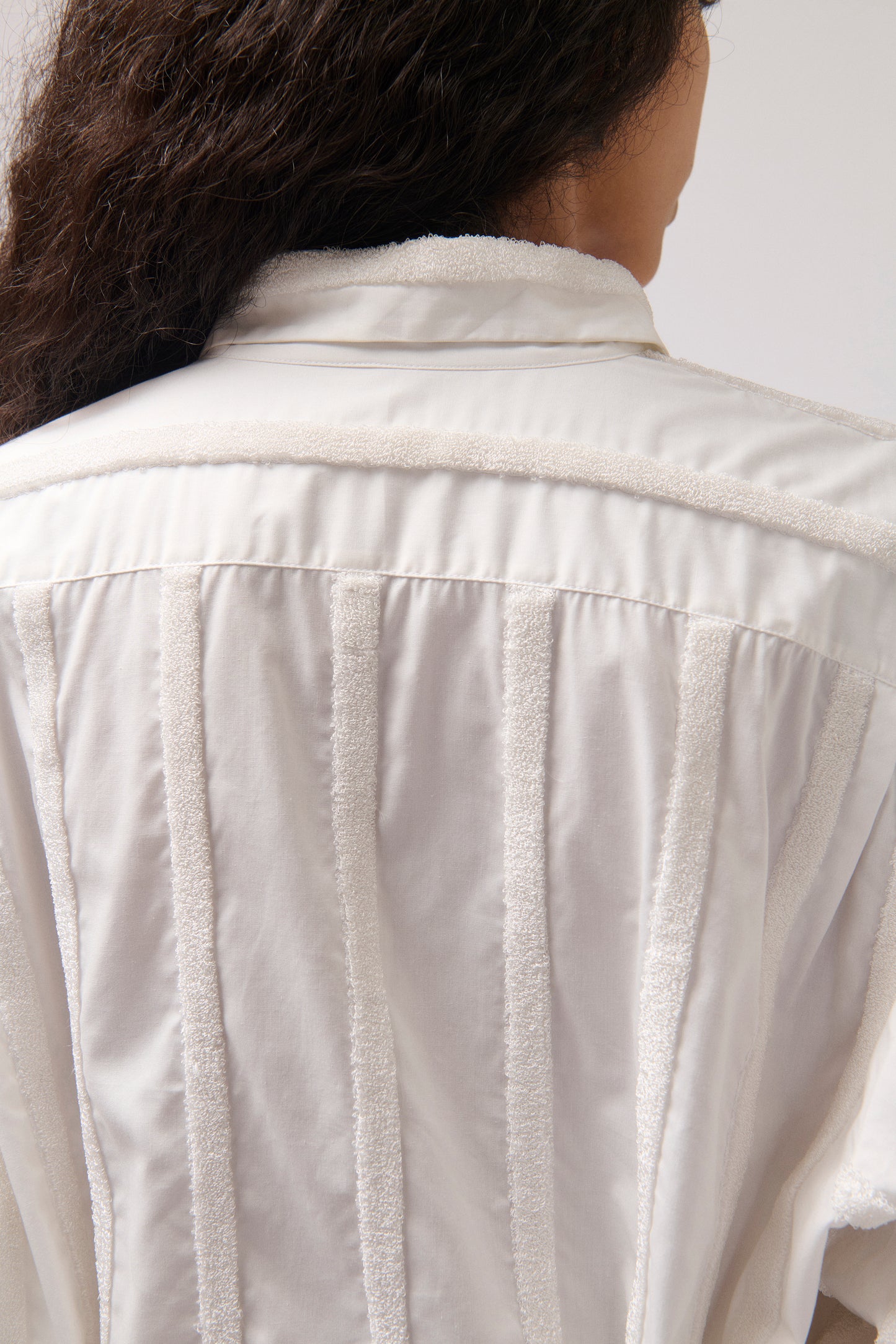 Close-up back view of a person wearing a white textured jacket with vertical stitched panels and a high collar.