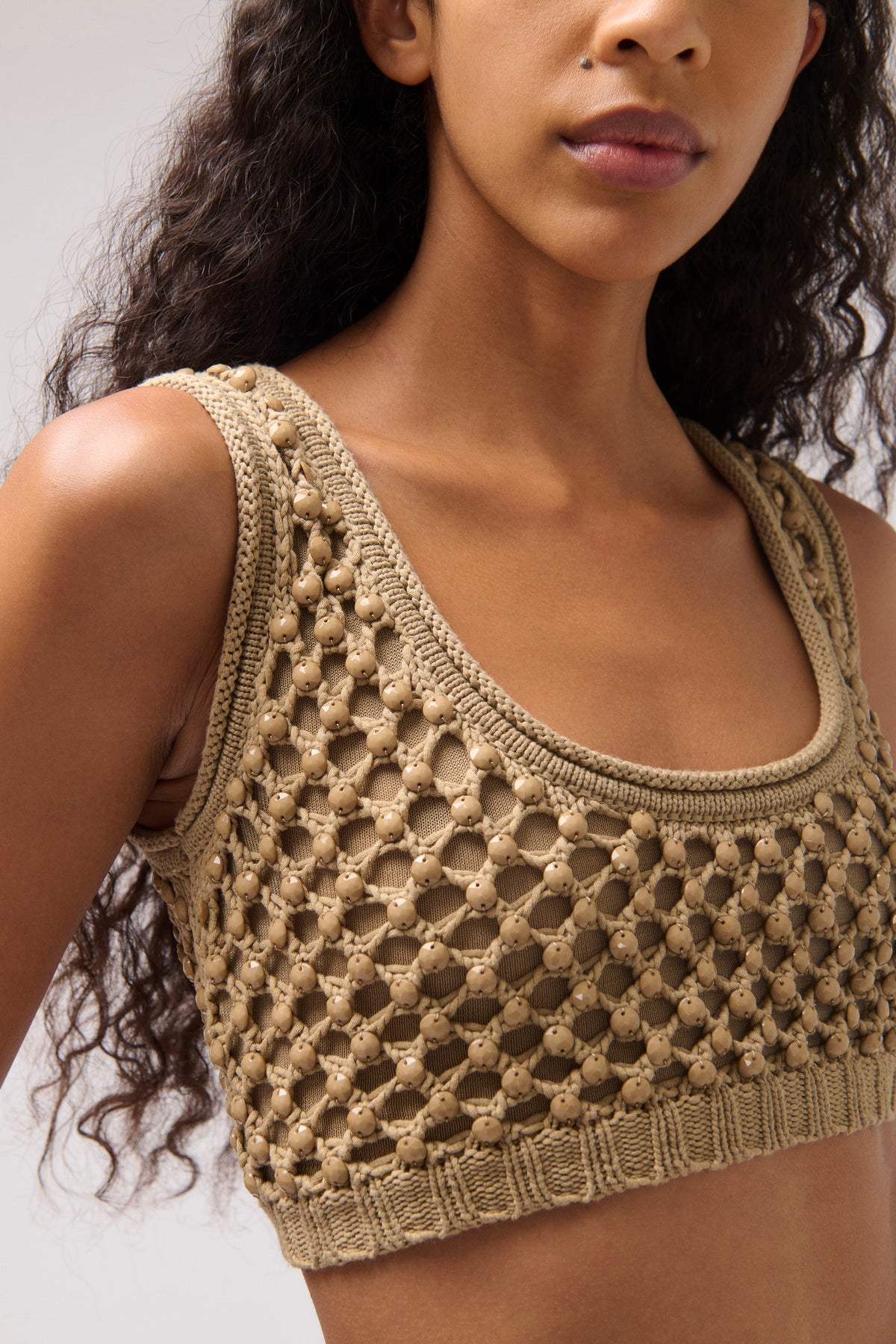 A close-up of a woman wearing a beige crochet knit crop top with a scoop neckline and textured openwork pattern.