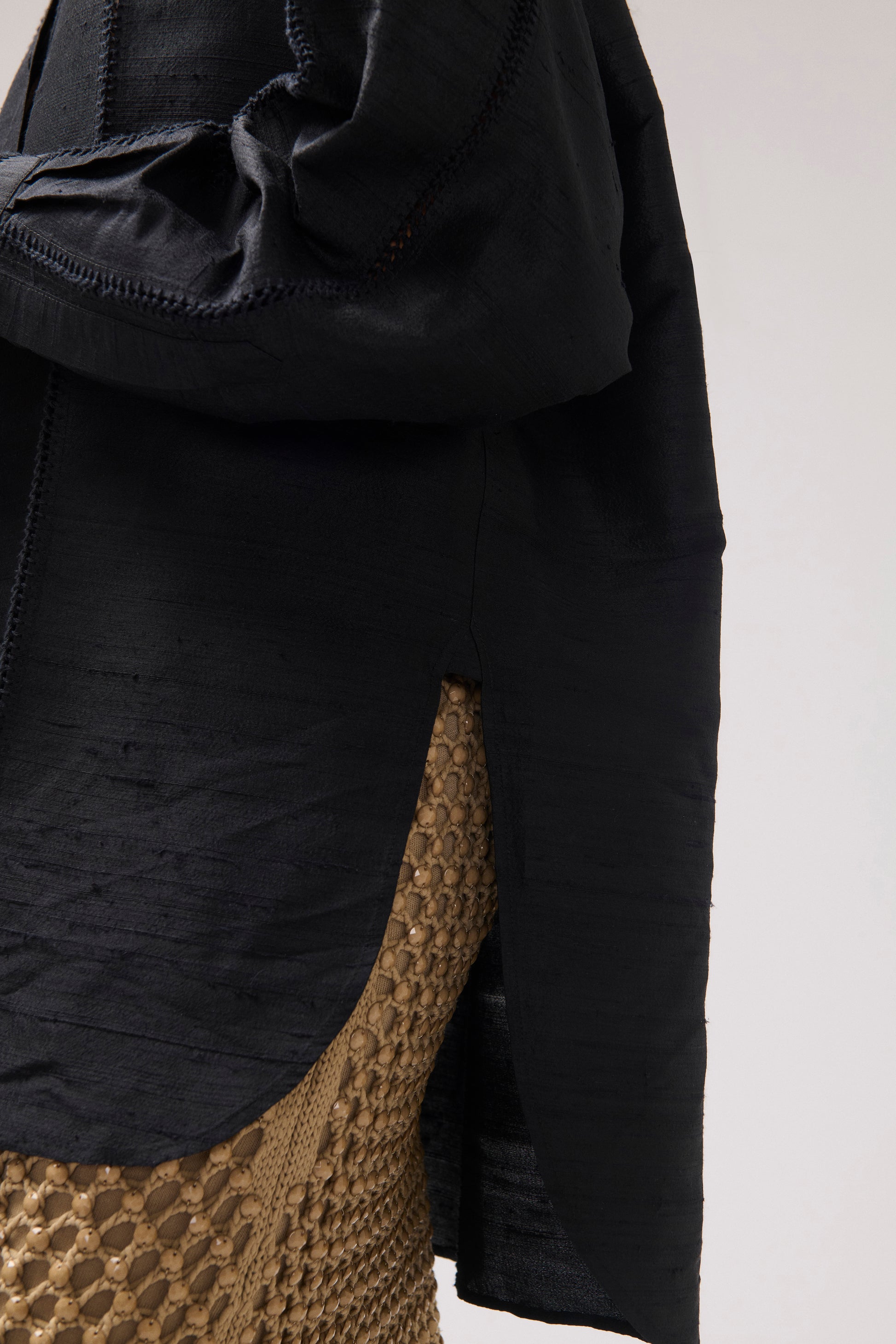 Close-up of a black textured silk shirt and a woven skirt shown against a plain light background.