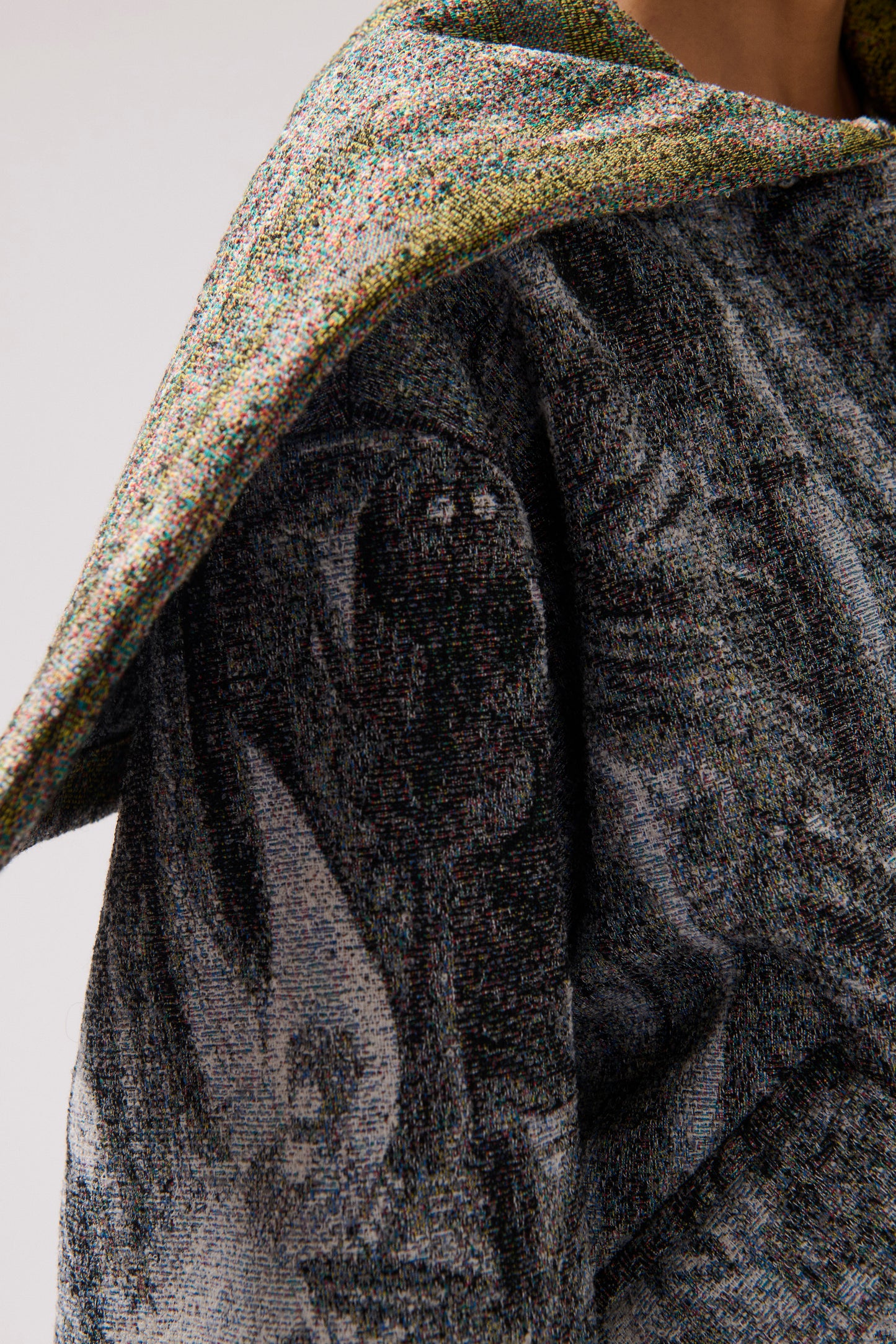 Close-up of a person wearing a long-sleeved, asymmetrical jacket with a gray, multi-color and white abstract print and a wide collar.