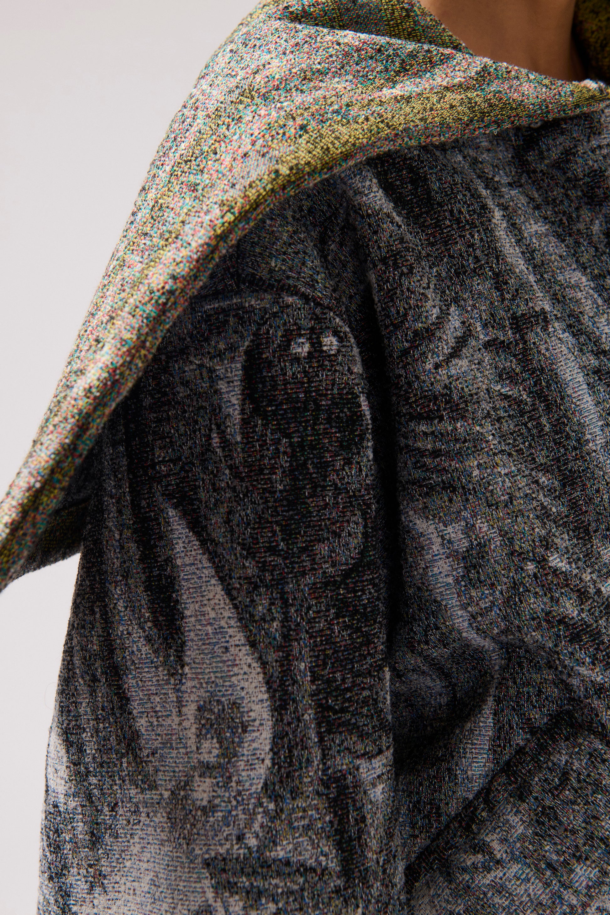 Close-up of a person wearing a long-sleeved, asymmetrical jacket with a gray, multi-color and white abstract print and a wide collar.