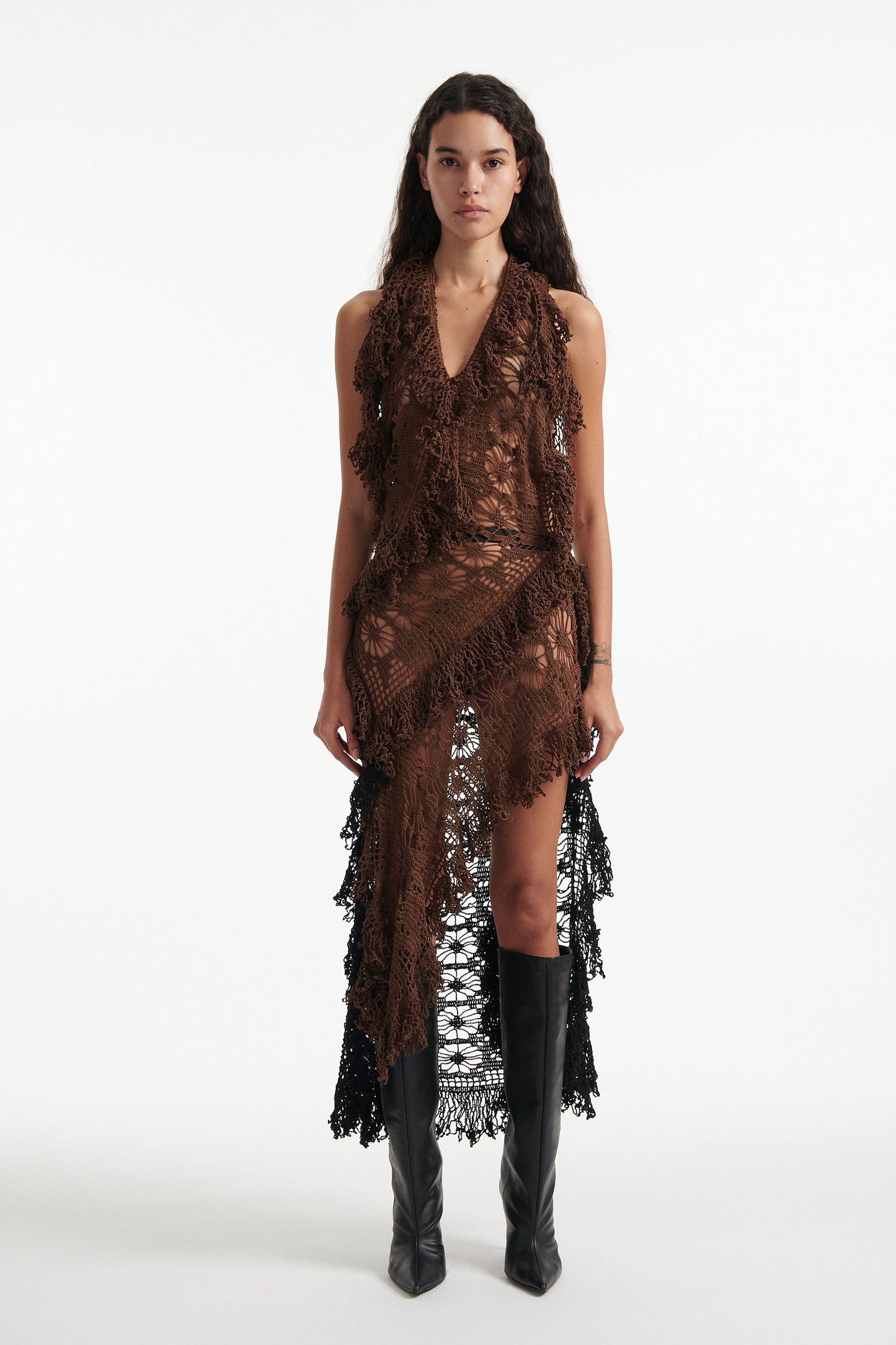 Female model wears open-back brown and black hand knit crochet dress with black high heels on white background. The front of the dress is brown and the back of the dress is black. 