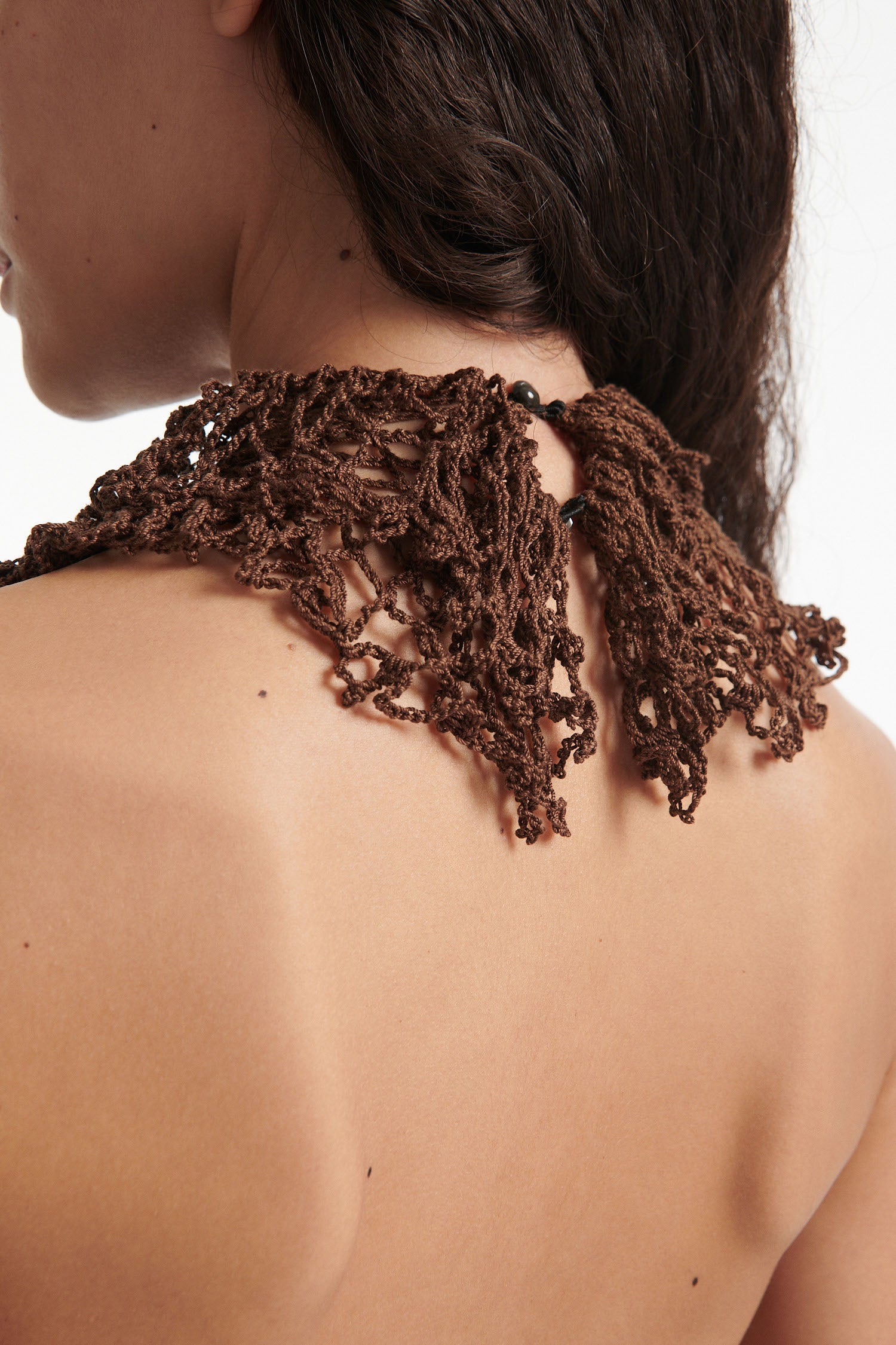 Female model wears open-back brown and black hand knit crochet dress with black high heels on white background. The front of the dress is brown and the back of the dress is black. 